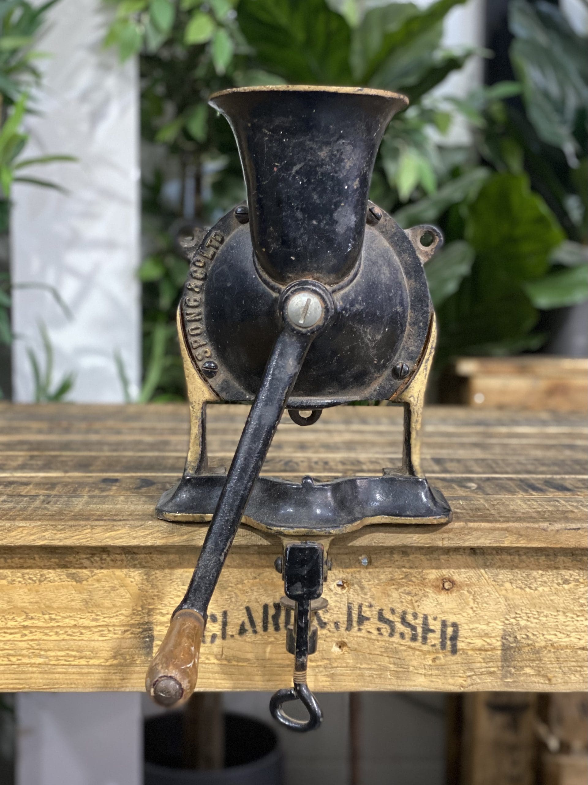 1856 No. 4 Large Spong & Co Ltd Bench Mounted Hand Grinder on a wooden table with greenery in the background.