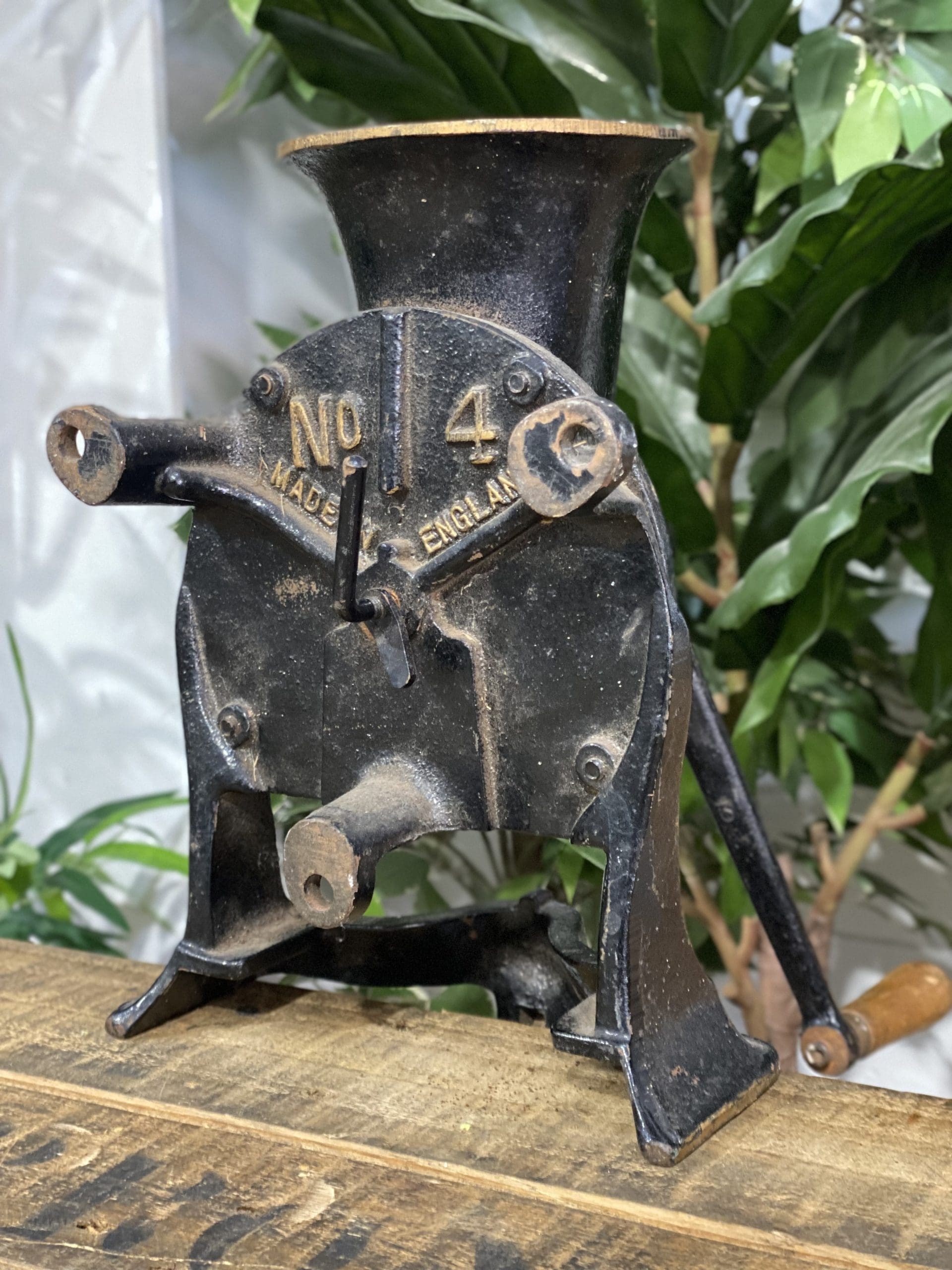 1856 No. 4 Large Spong & Co Ltd Bench Mounted Hand Grinder displayed on wooden table with green foliage in background.
