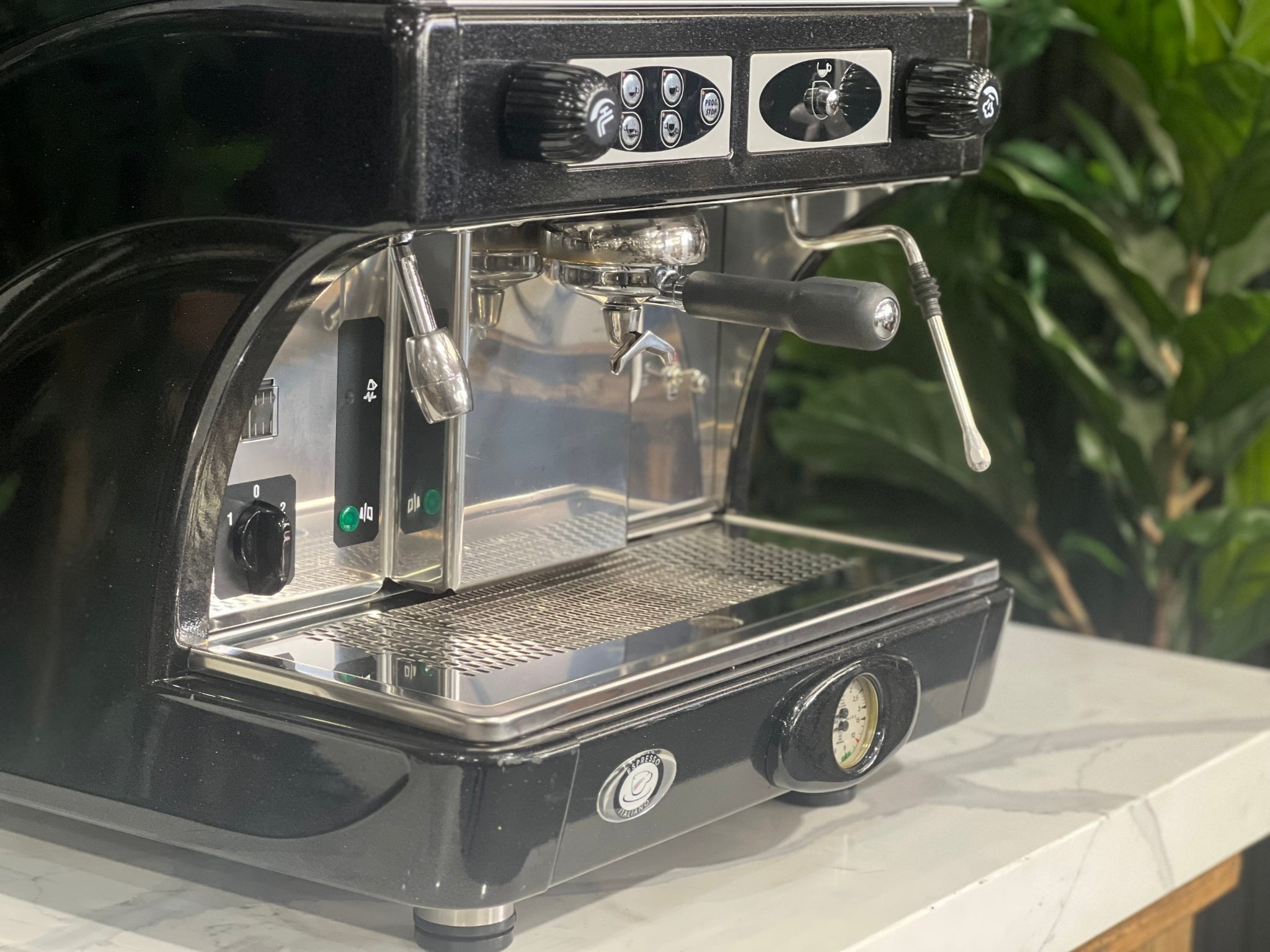 Astoria Calypso 1 Group Black Espresso Coffee Machine sitting on a marble bench with greenery in the background. Image is taken from an angle so that the front and side of machine is visible. The image is a close up image of the buttons, steam want and group handle