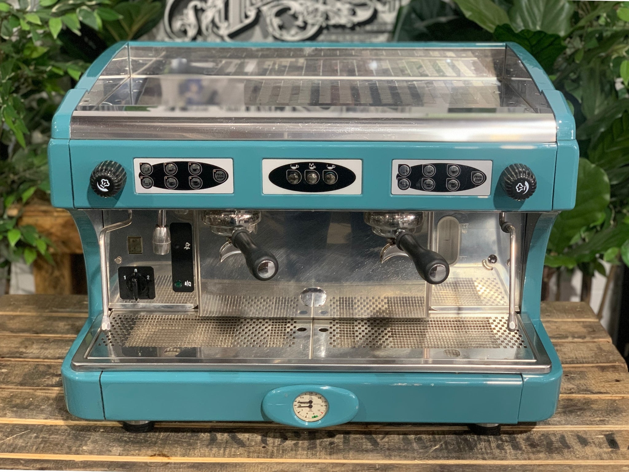 Astoria Calypso 2 Group Aqua Espresso Coffee Machine sitting on a wooden bench. Front on image and the top of the machine is visible