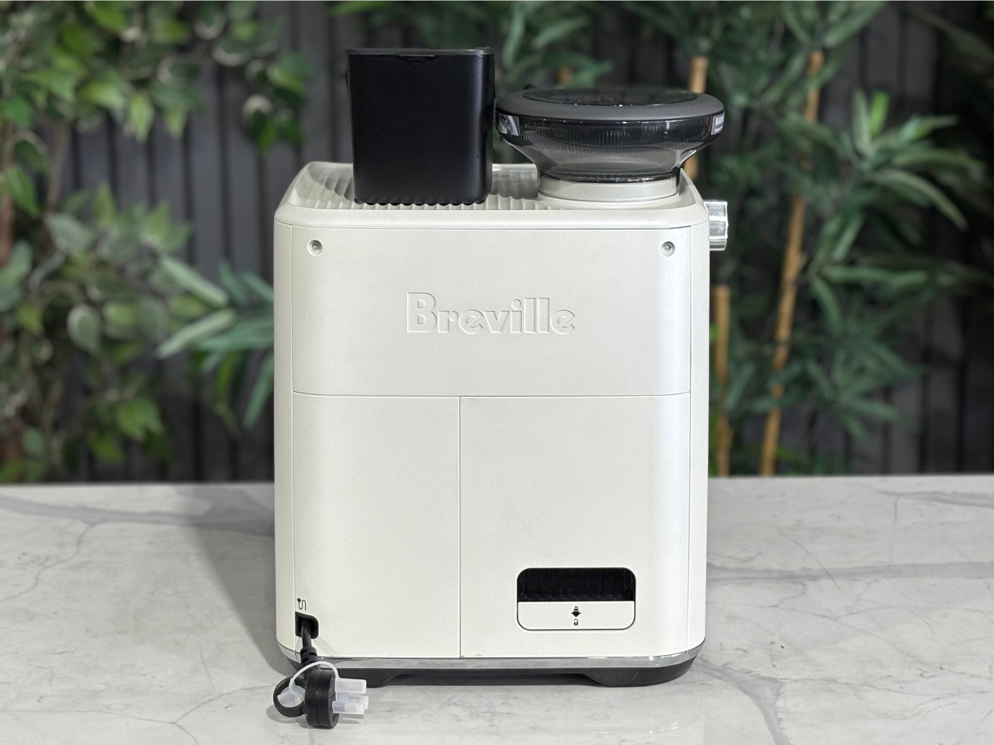 Breville Oracle Jet 1 Group Coffee Machine White - New, rear view on a marble bench, showing the white body and power connection area of this premium espresso coffee machine with greenery in the background.