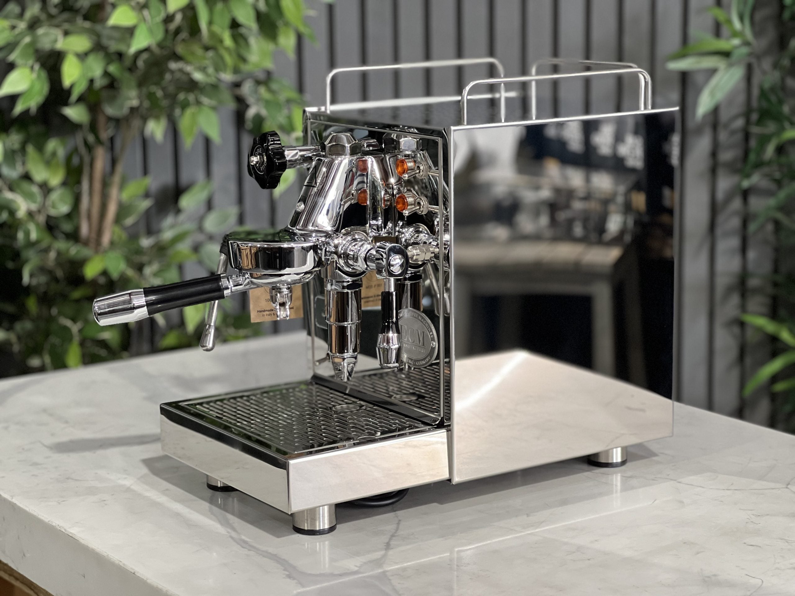 ECM Classika PID 1 Group Coffee Machine Stainless - New espresso coffee machine, side-on view showing the E61 group head, stainless steel steam wand, and sleek body design, on a white marble counter with green plants behind.
