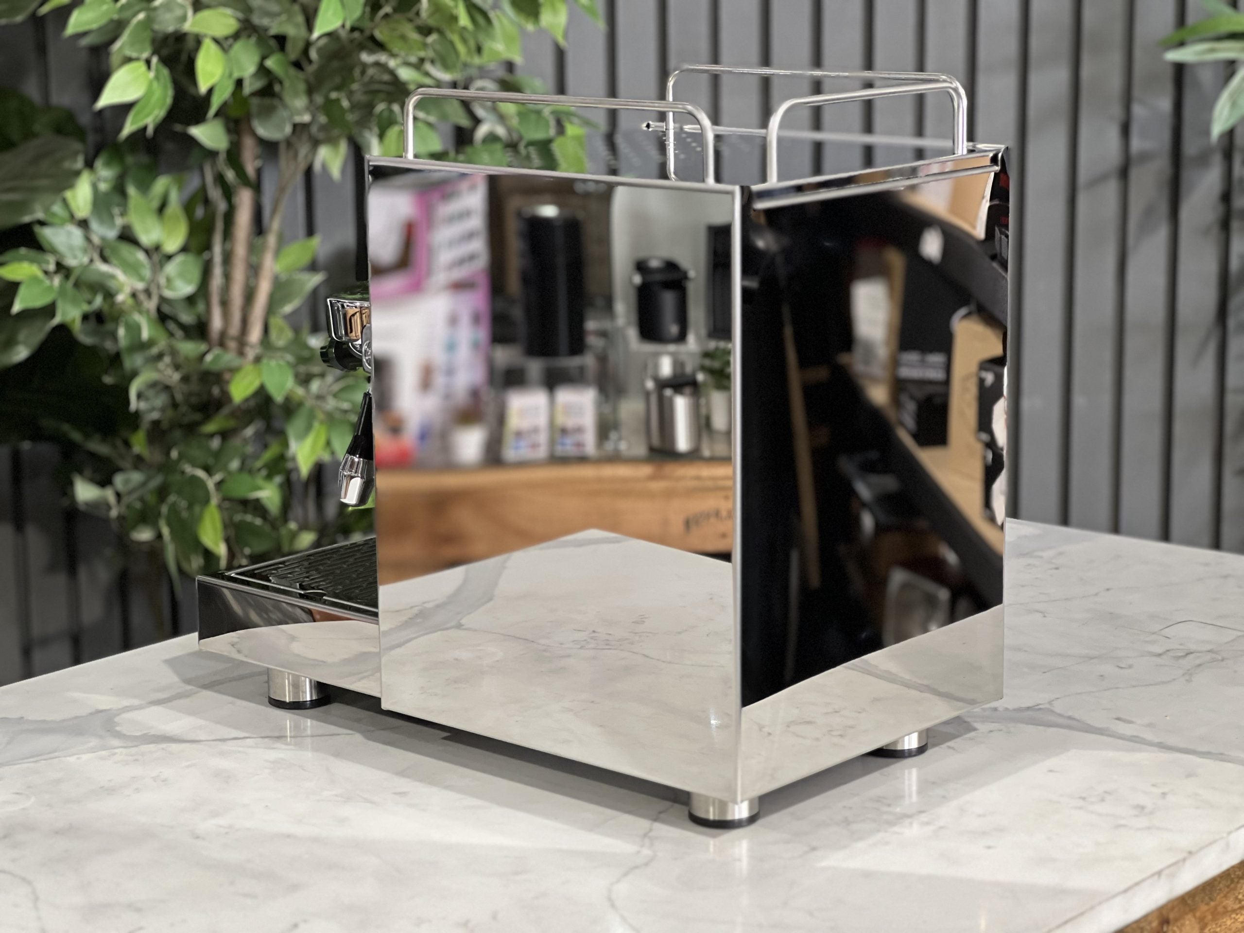 ECM Classika PID 1 Group Coffee Machine Stainless - New espresso coffee machine, angled rear view showing the water tank and overall compact design, positioned on a white marble bench with greenery in the background.