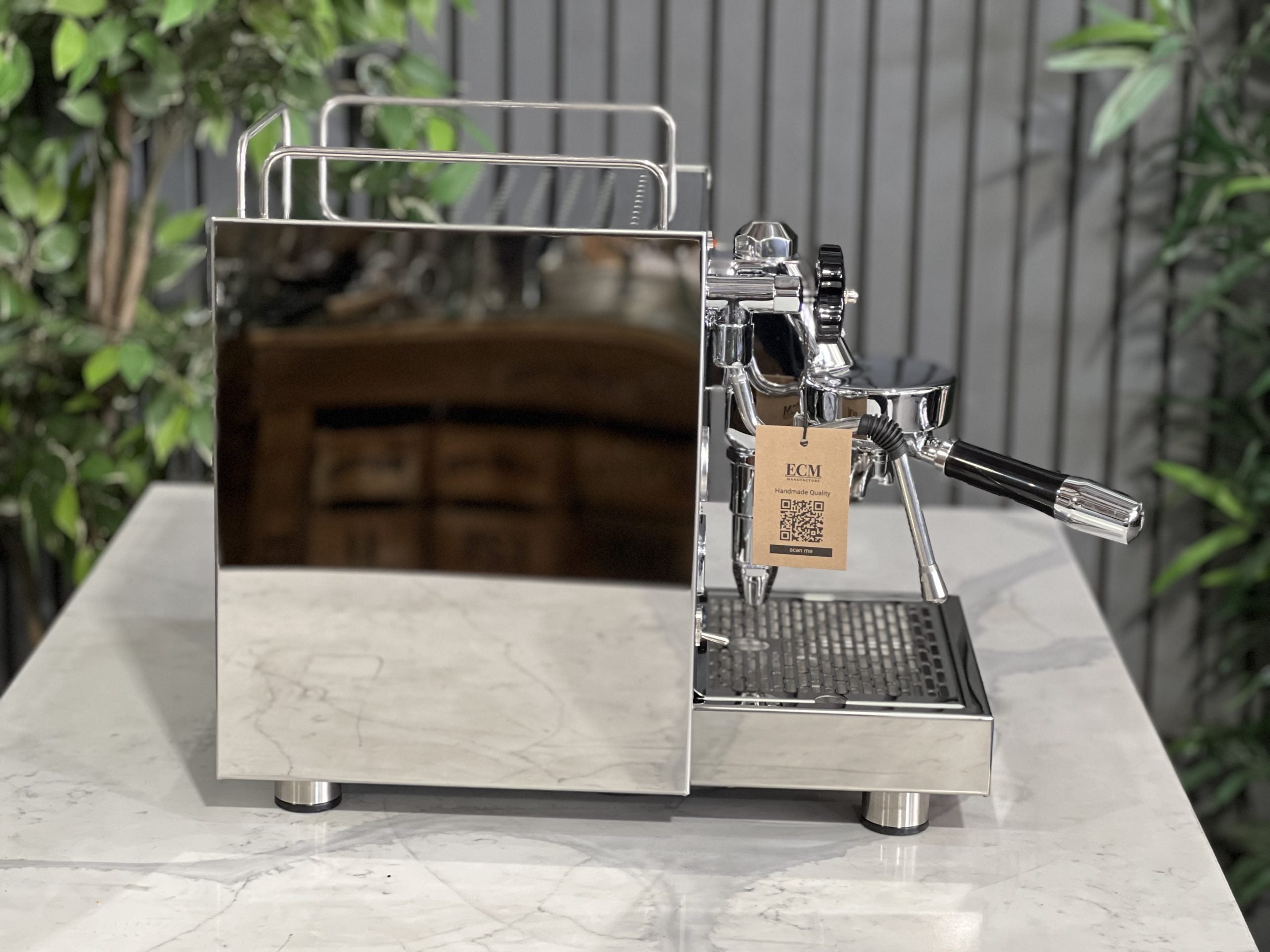 ECM Classika PID 1 Group Coffee Machine Stainless - New espresso coffee machine, side-on view showing the E61 group head, stainless steel steam wand, and sleek body design, on a white marble counter with green plants behind.