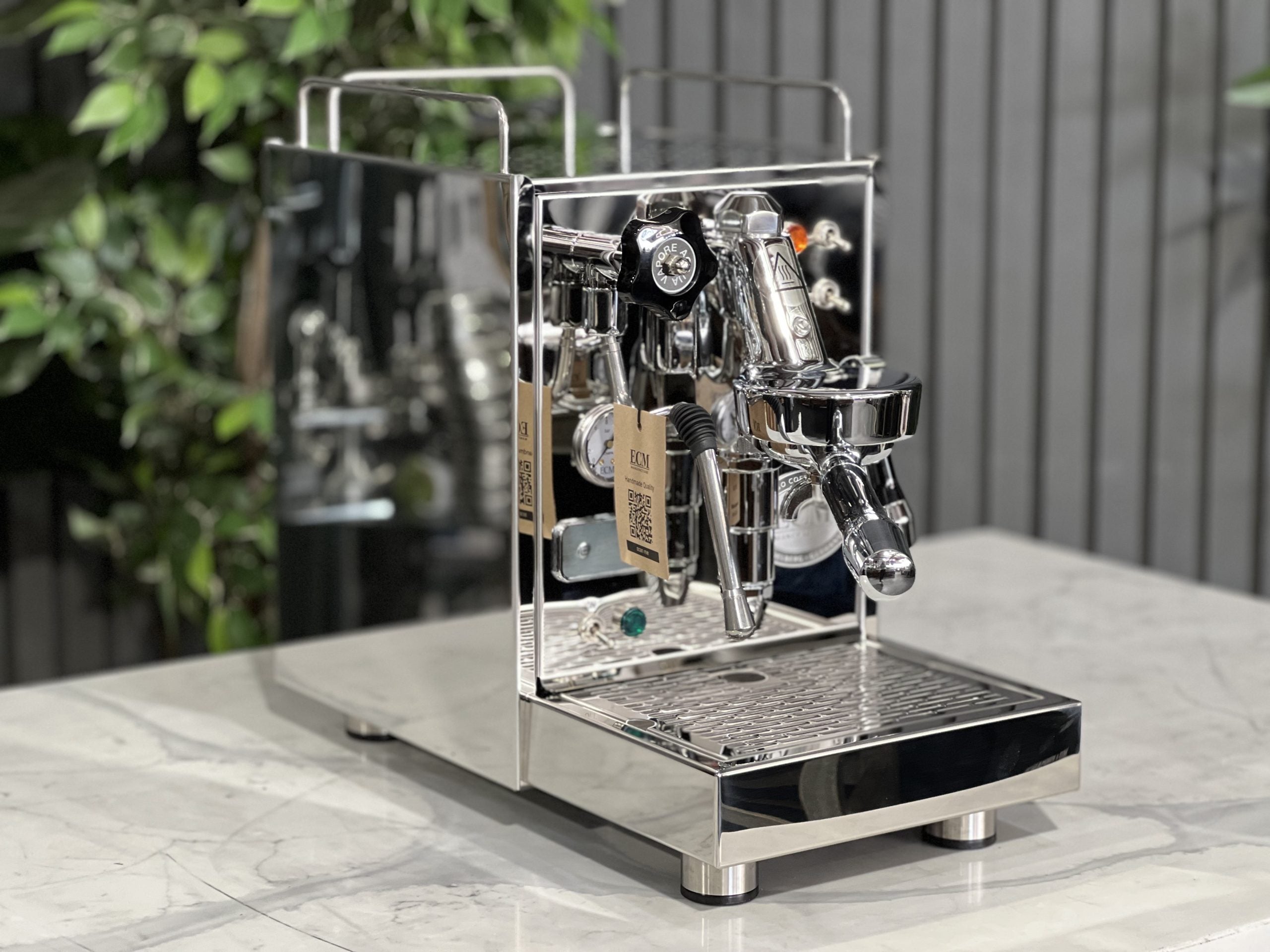 ECM Classika PID 1 Group Coffee Machine Stainless - New espresso coffee machine, angled view showing the E61 group head, steam wand, and cup warming tray, placed on a white marble bench with greenery in the background.