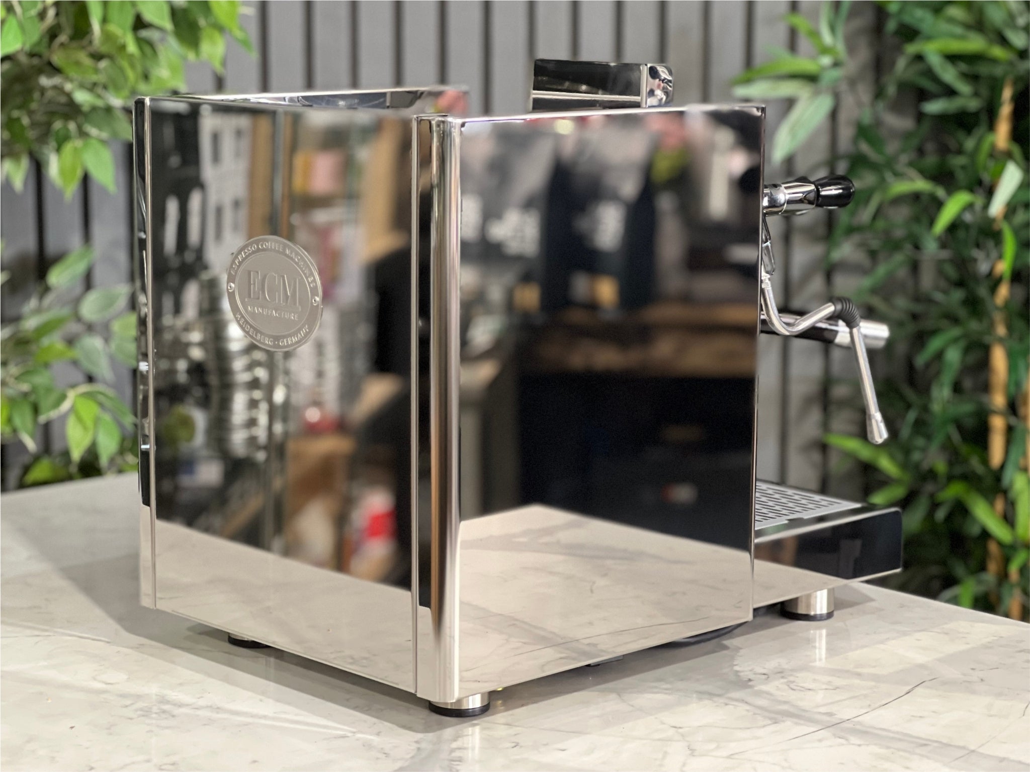 ECM Elektronika II Profi Rotary 1 Group Espresso Coffee Machine Stainless – New, angled rear view showing the stainless steel body and overall design on a marble bench with greenery behind.