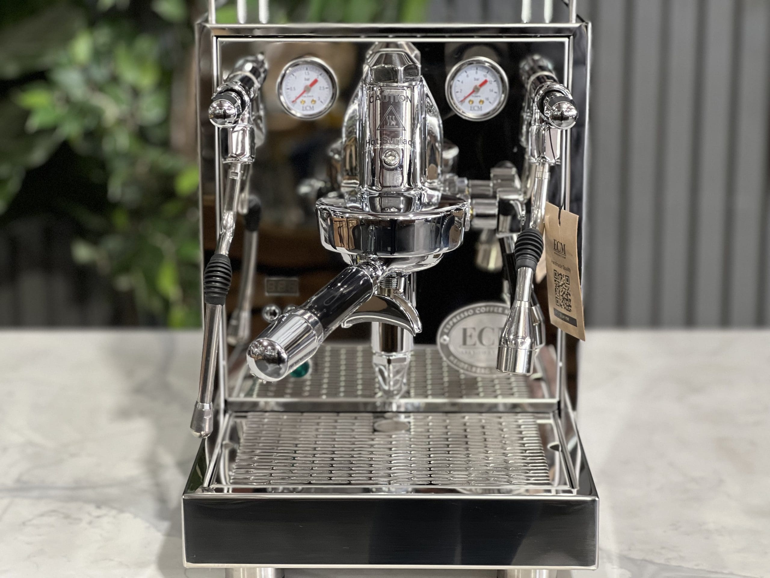 Front view of the ECM Mechanika Max Rotary 1 Group Espresso Coffee Machine Stainless - New on a white marble bench with greenery behind, showcasing the classic E61 group head, dual flick taps, and stainless steel finish.