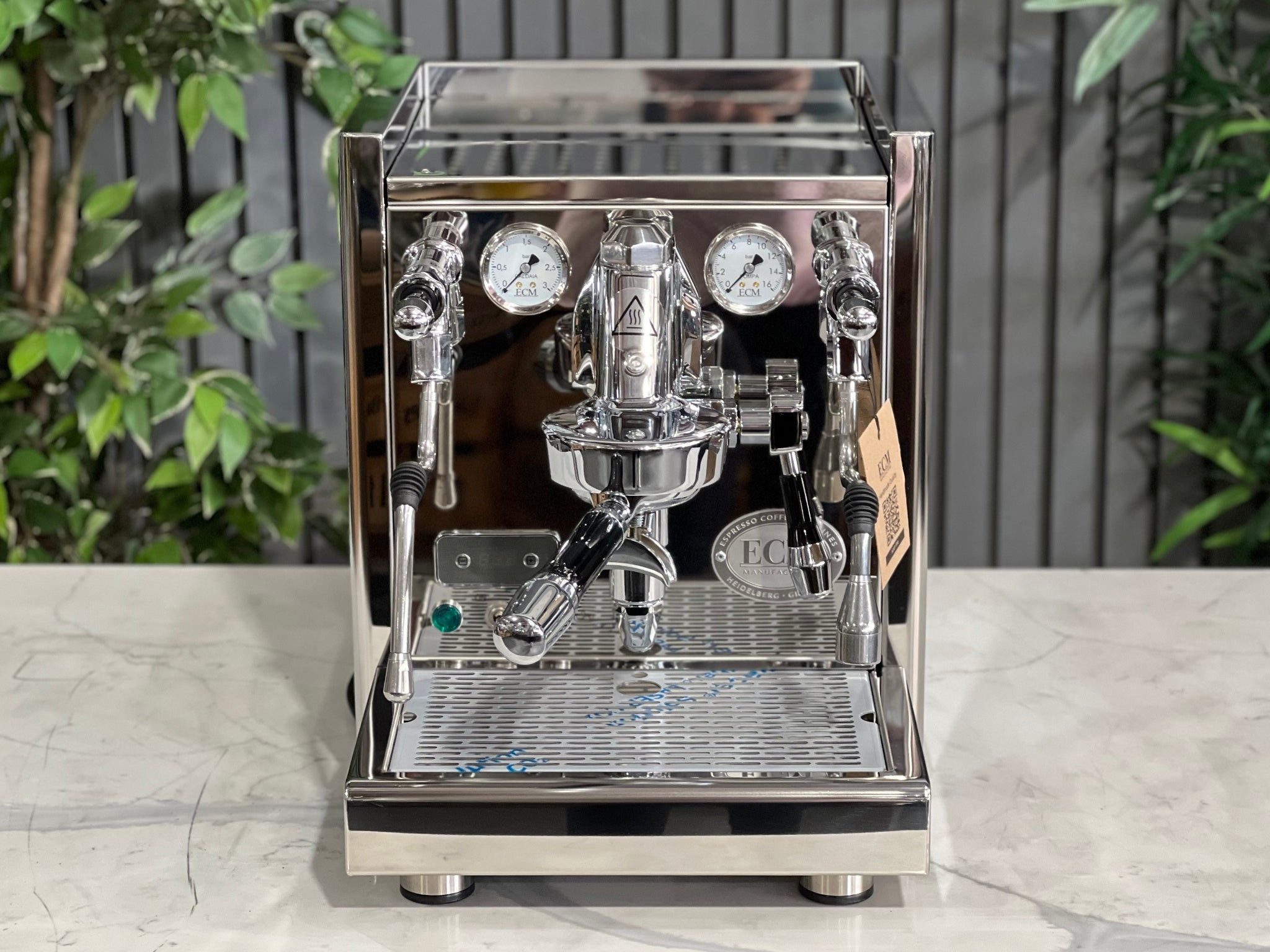 ECM Technika V Profi Rotary PID 1 Group Coffee Machine Stainless – New espresso coffee machine viewed from the front with the top visible, featuring the cup-warming tray, E61 group head, and stainless body on a marble bench with greenery behind.