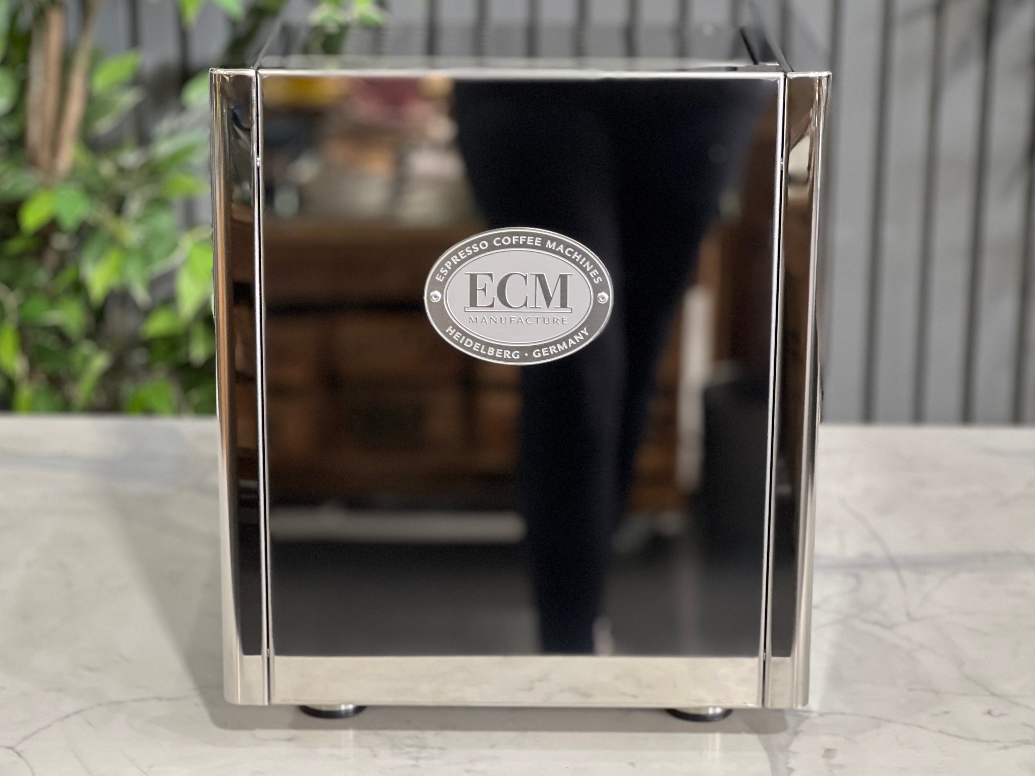 Rear view of the ECM Technika V Profi Rotary PID 1 Group Coffee Machine Stainless – New espresso coffee machine on a white marble bench with greenery behind, showing the polished stainless steel back panel and ventilation design.