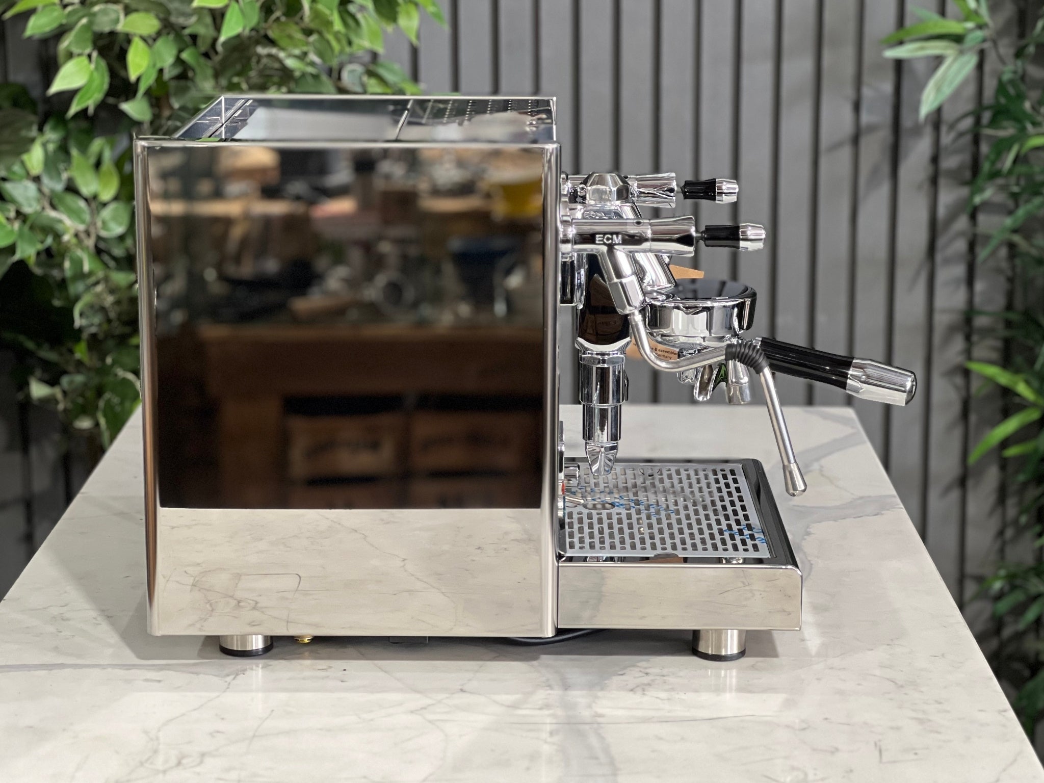 Side profile of the ECM Technika V Profi Rotary PID 1 Group Coffee Machine Stainless – New espresso coffee machine on a marble bench with greenery behind, highlighting the mirror-finish side panels, steam wand, and classic ECM design.