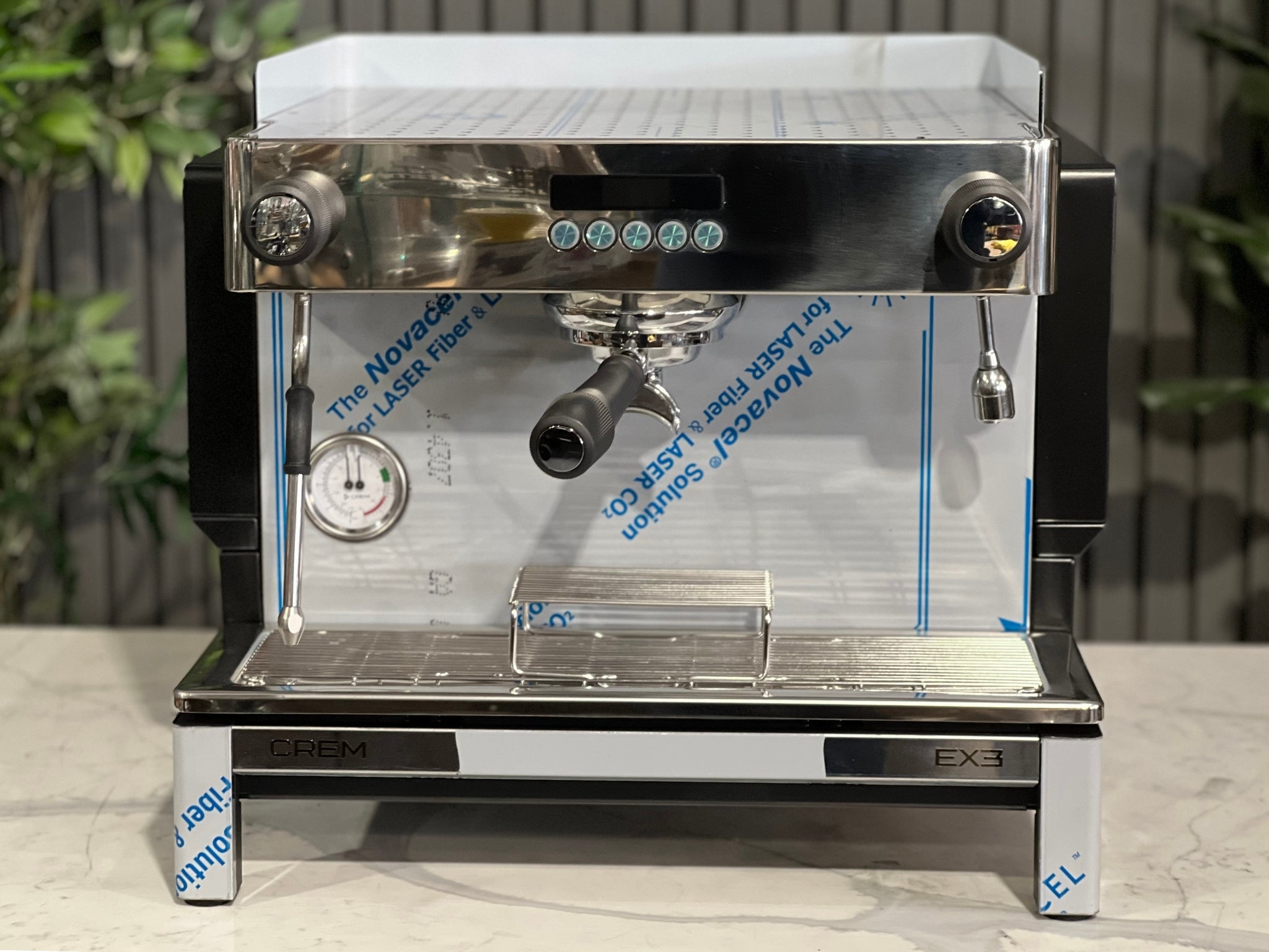 Expobar Crem EX3 Compact 1 Group Coffee Machine Black - New front-facing image highlighting the group head, PID-controlled panel, and volumetric buttons, set on a marble bench with greenery behind. A modern espresso machine with precision brewing features.