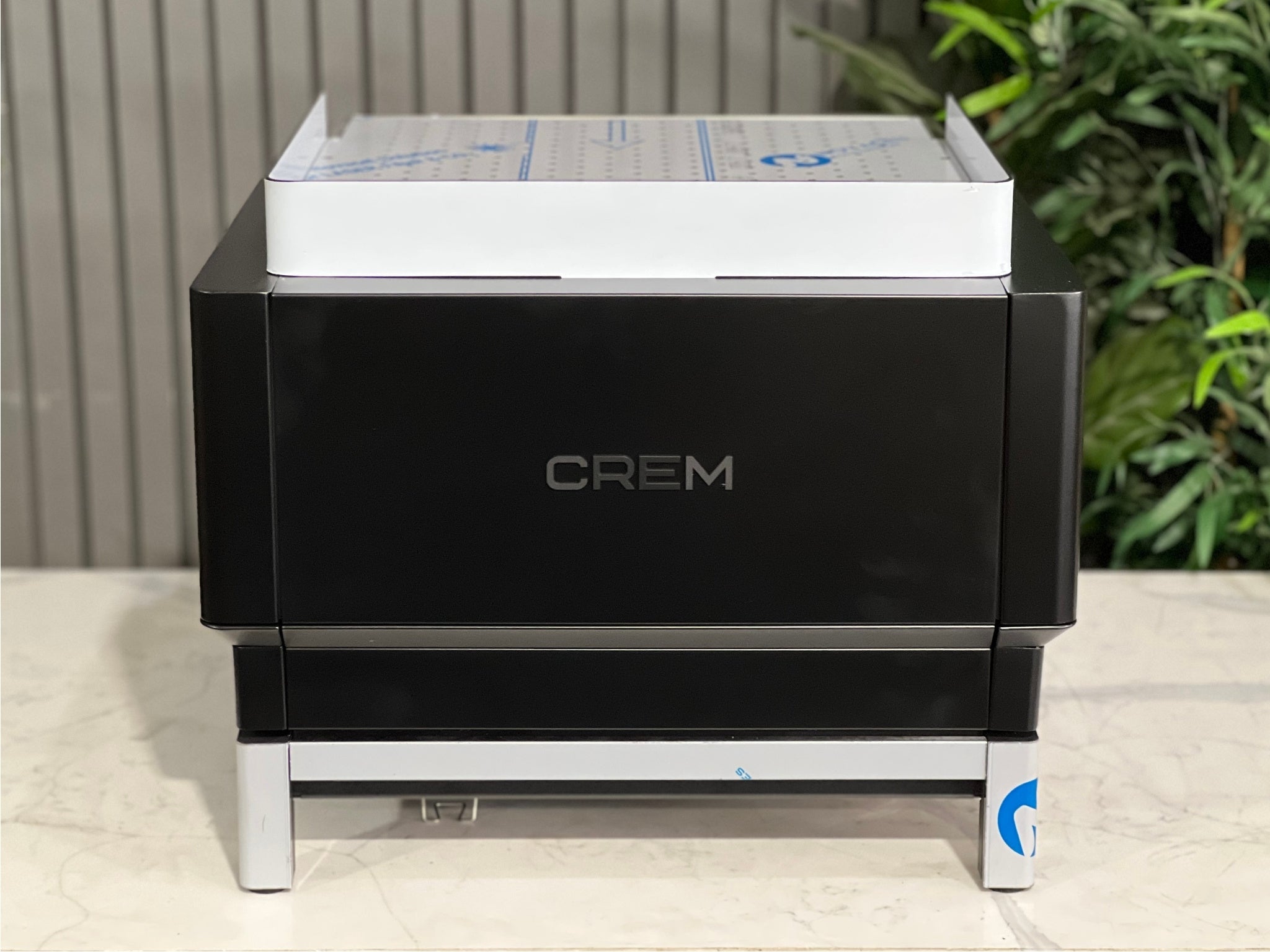 Expobar Crem EX3 Compact 1 Group Coffee Machine Black - New rear view showing the back panel and overall compact shape. The black finish stands out against the marble bench and greenery, perfect for modern espresso setups.