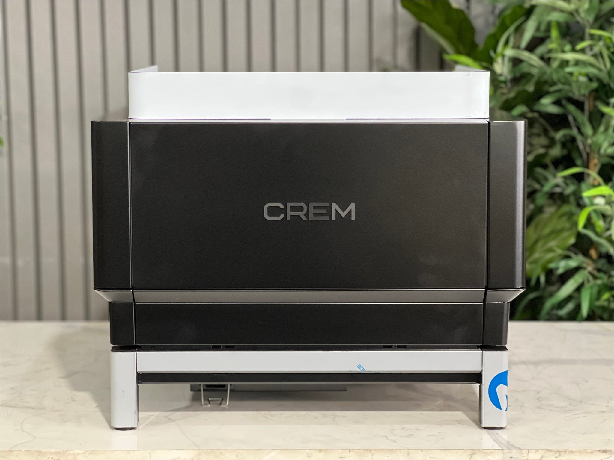 Expobar Crem EX3 Compact 1 Group Coffee Machine Black - New rear view showing the back panel and overall compact shape. The black finish stands out against the marble bench and greenery, perfect for modern espresso setups.