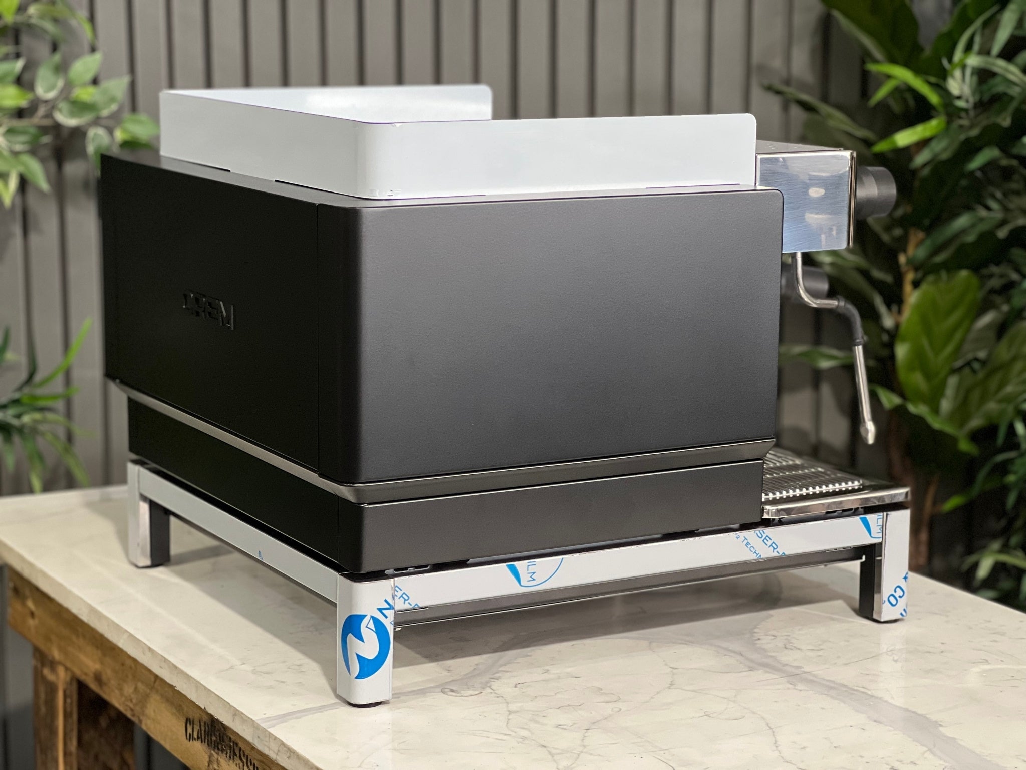 Expobar Crem EX3 Compact 1 Group Coffee Machine Black - New angled rear image showing the curvature of the frame and the compact footprint of the espresso machine. The black finish contrasts beautifully with the marble bench and green background.