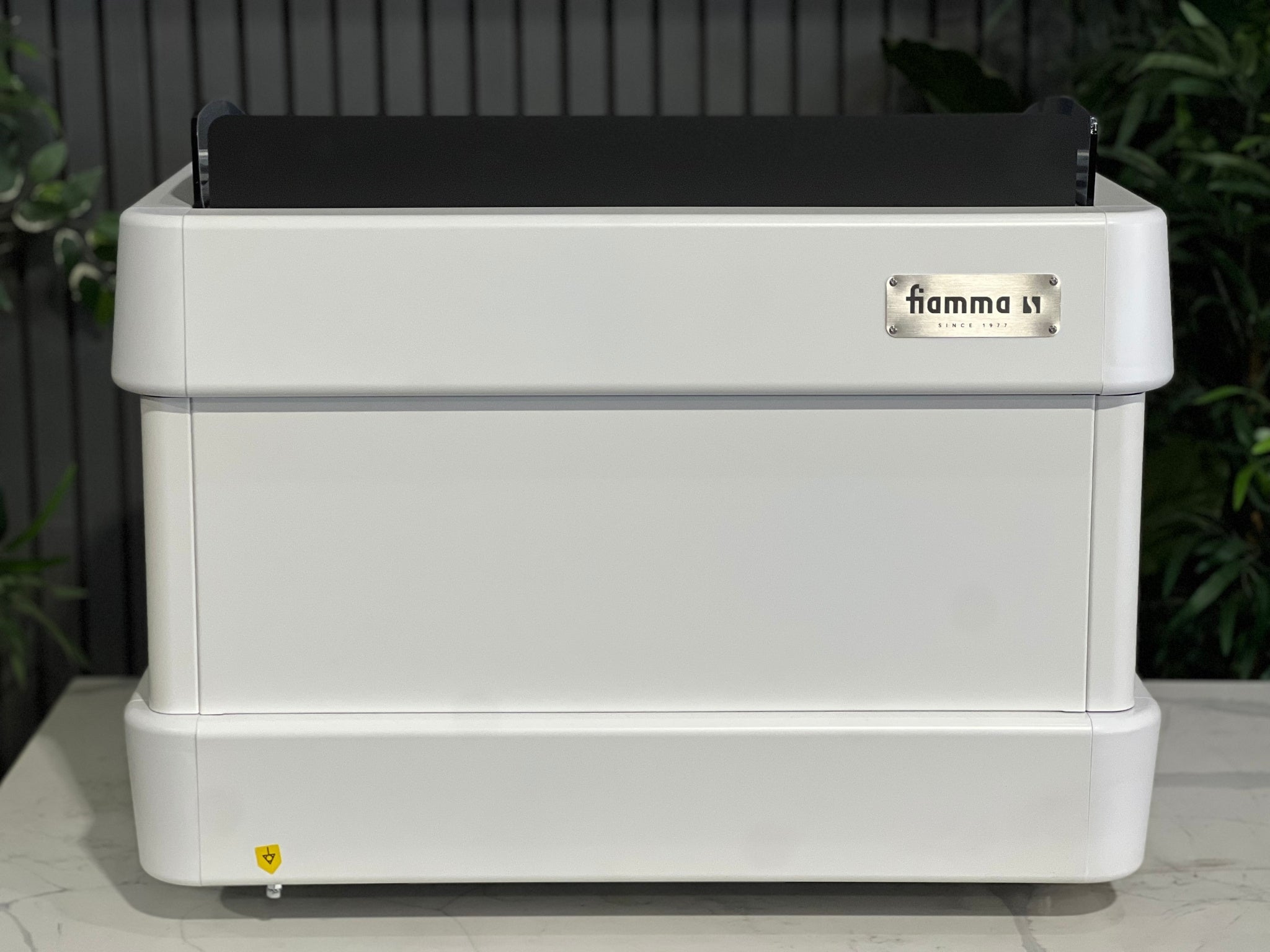 l is sitting on a marble bench. There is greenery in the background. The image is taken from behind the machine so the back is visible.