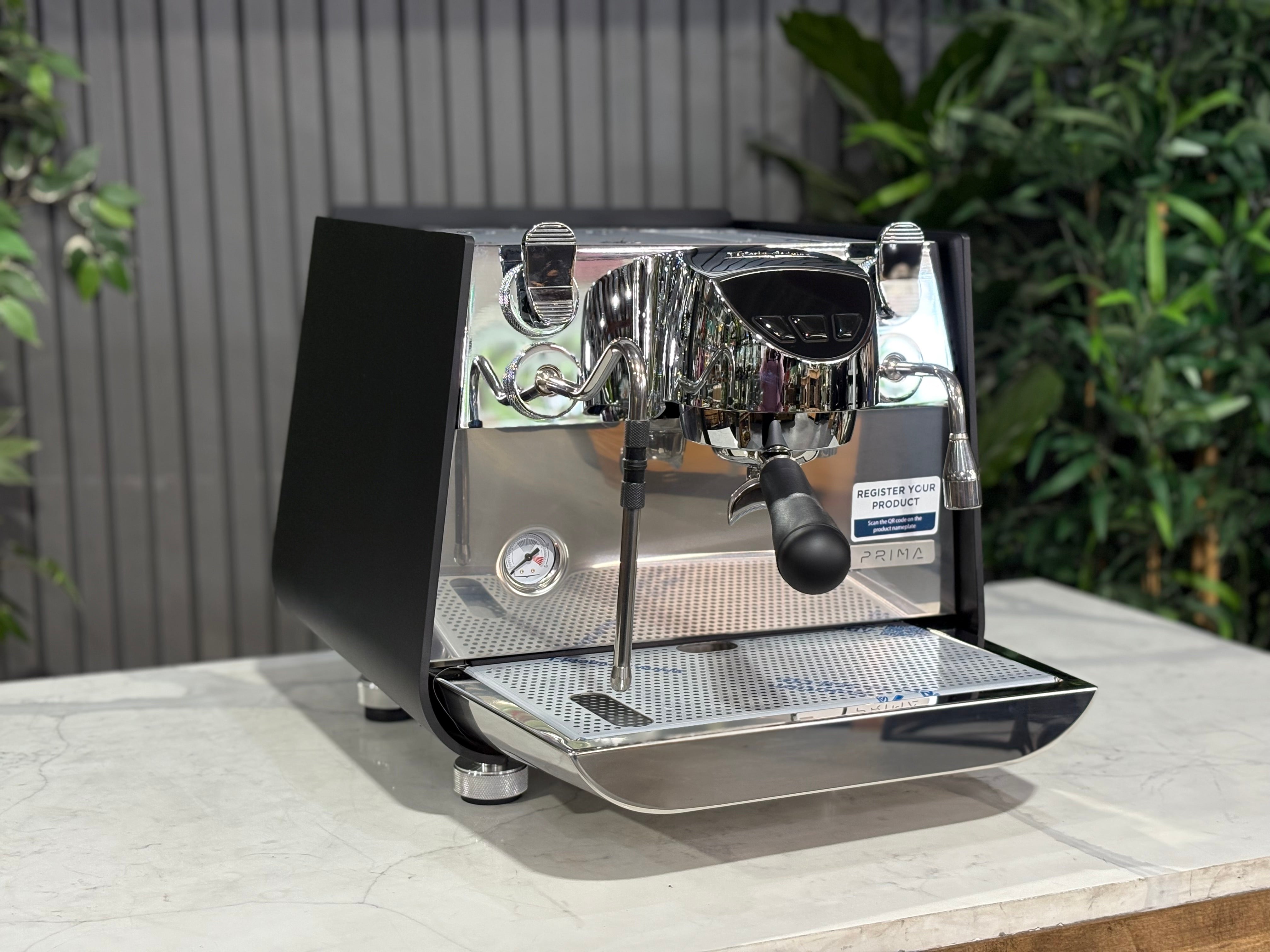 Victoria Arduino Eagle One Prima 1 Group Coffee Machine Black on a countertop with green plants in the background.