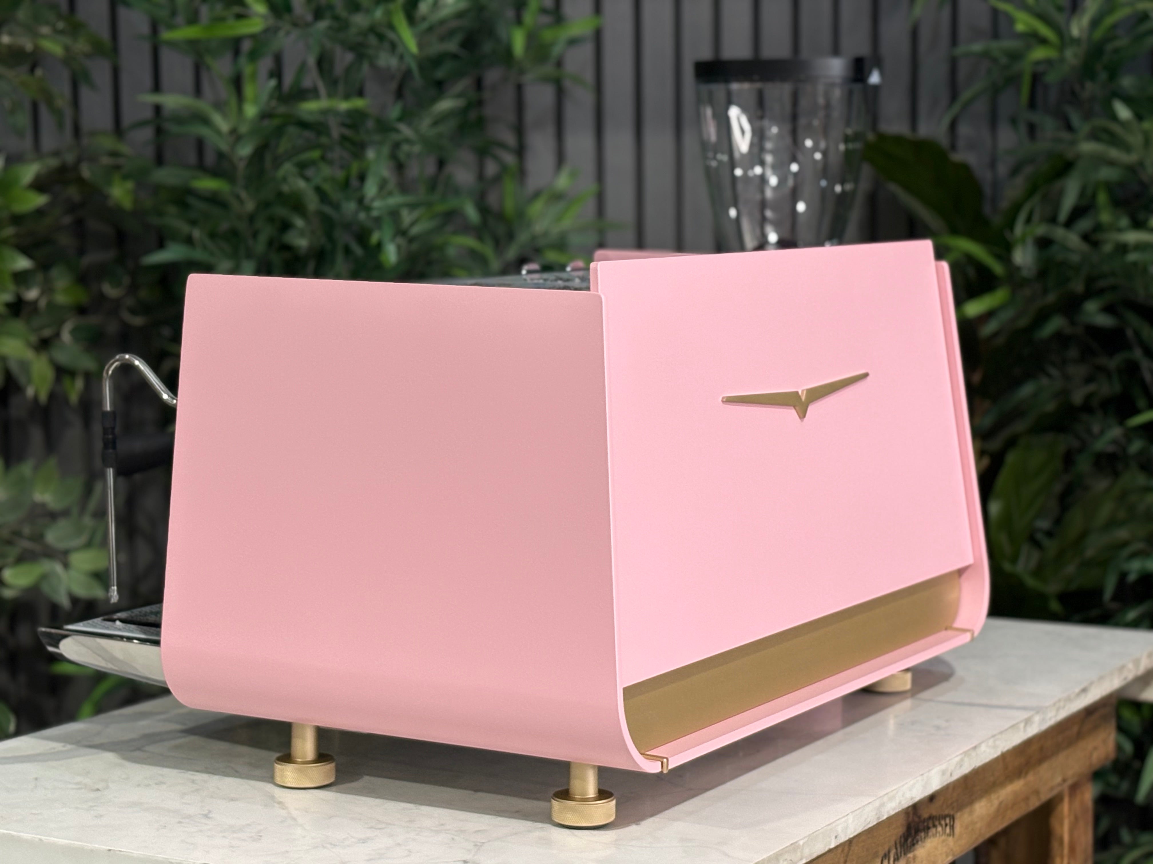 Victoria Arduino Eagle One 2 Group Coffee Machine Custom Pink & Gold displayed on a wooden counter with greenery in background.