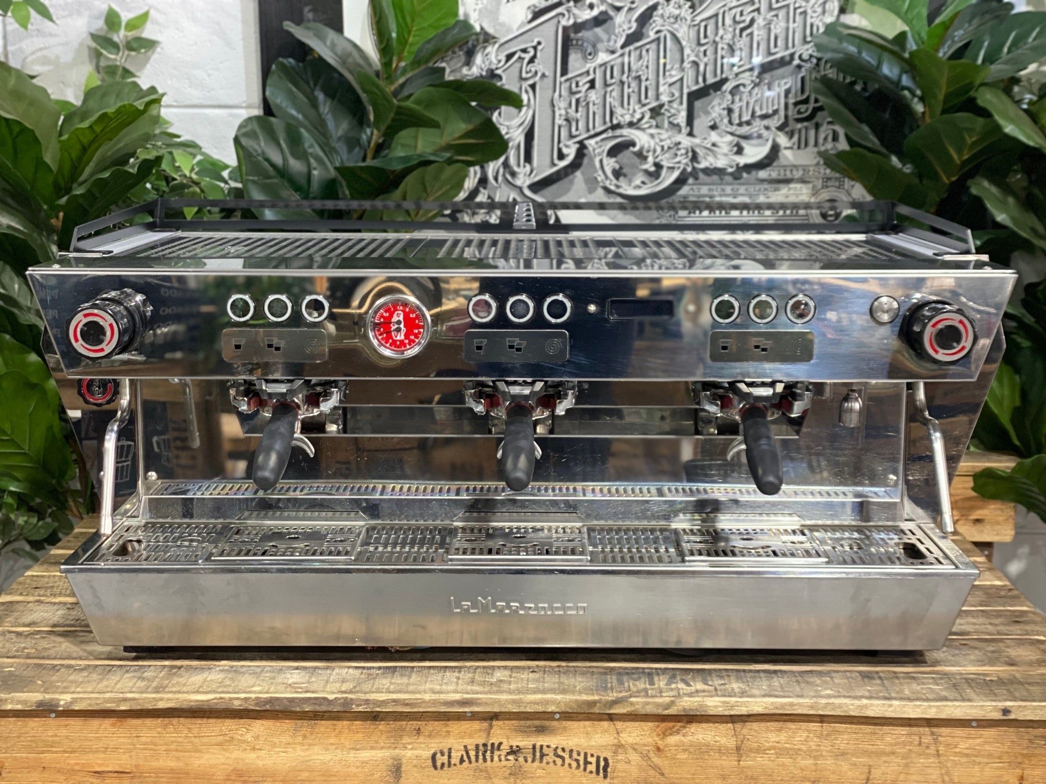 La Marzocco KB90 ABR 3 Group Coffee Machine White front view showcasing the straight-in portafilters, integrated ABR scales, and high cup clearance ideal for espresso service, with a natural backdrop of greenery.