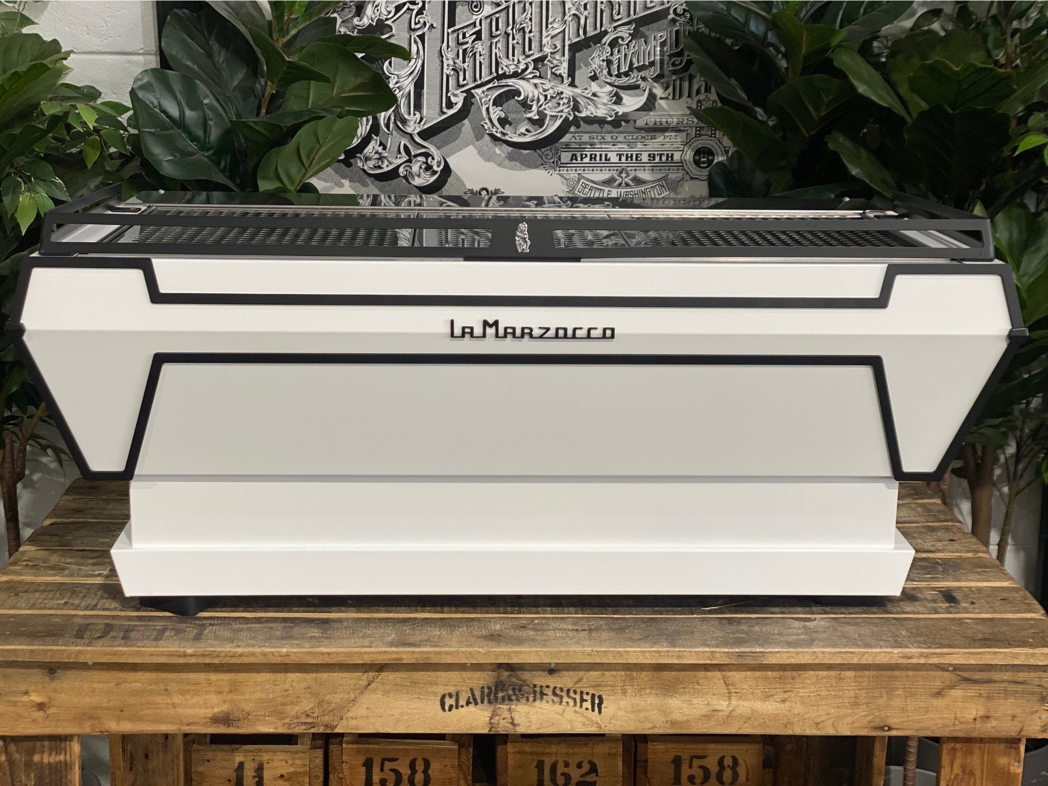 La Marzocco KB90 ABR 3 Group Coffee Machine White rear view showing the clean white back panel and sleek profile of this commercial espresso coffee machine, set against a backdrop of greenery.