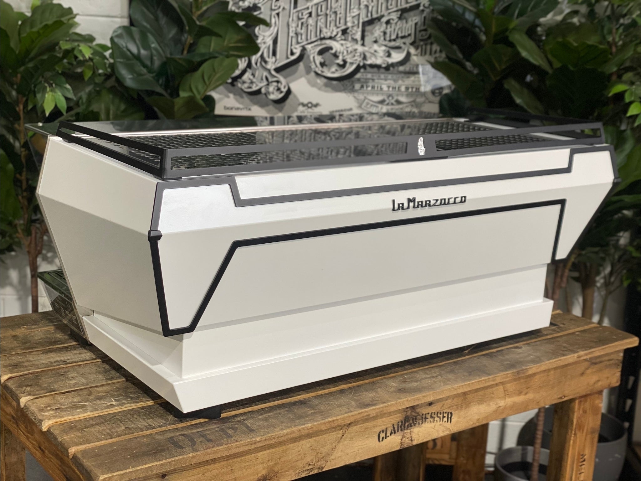 La Marzocco KB90 ABR 3 Group Coffee Machine White angled rear view displaying the stylish white casing and robust commercial build of this 3 group espresso machine, captured outdoors with greenery behind.