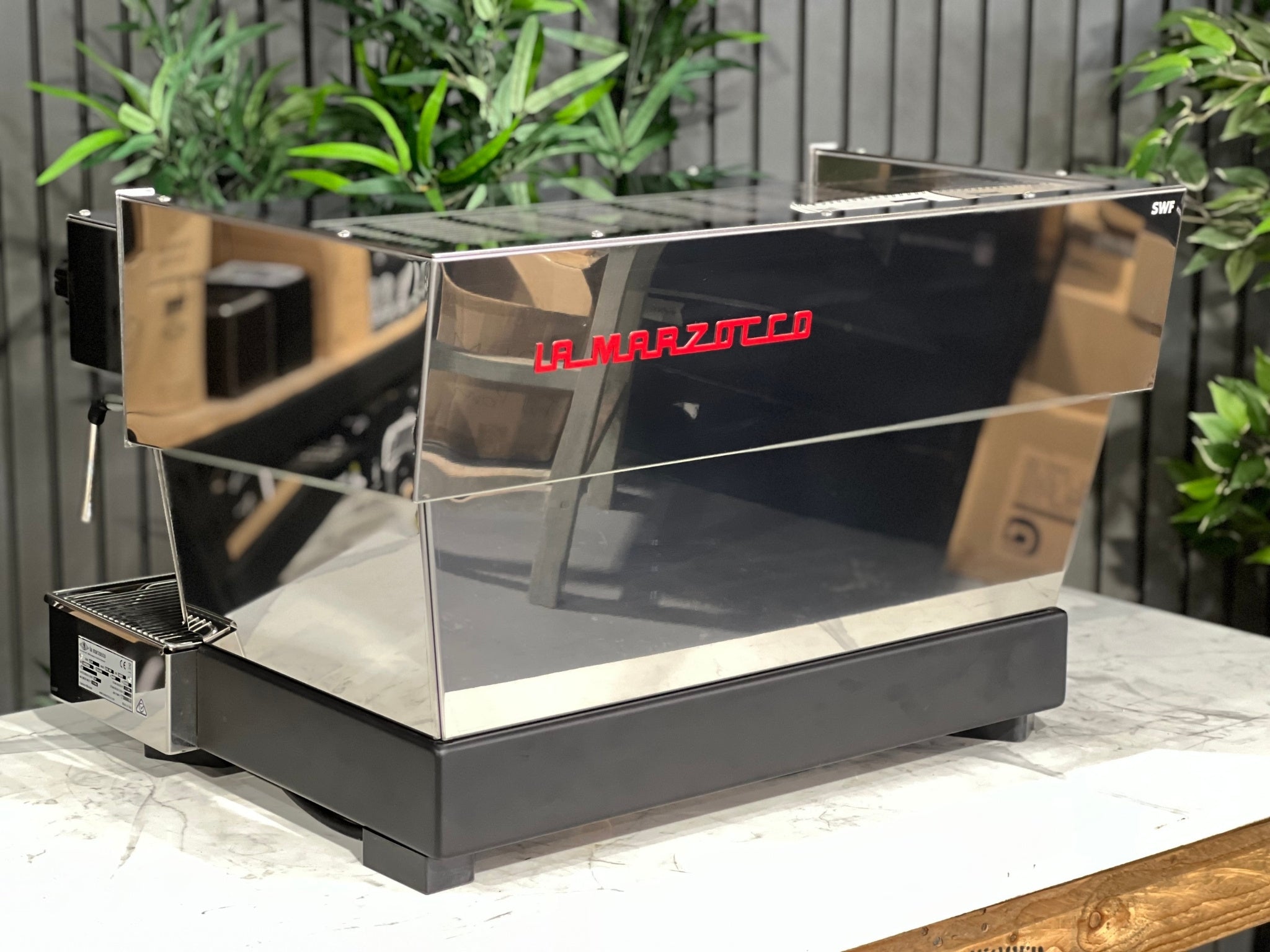 La Marzocco Linea Classic S AV 2 Group Coffee Machine Stainless - New angled back view showing the boiler system and rear structure, showcasing the stainless steel finish, on a marble bench with greenery in the background.