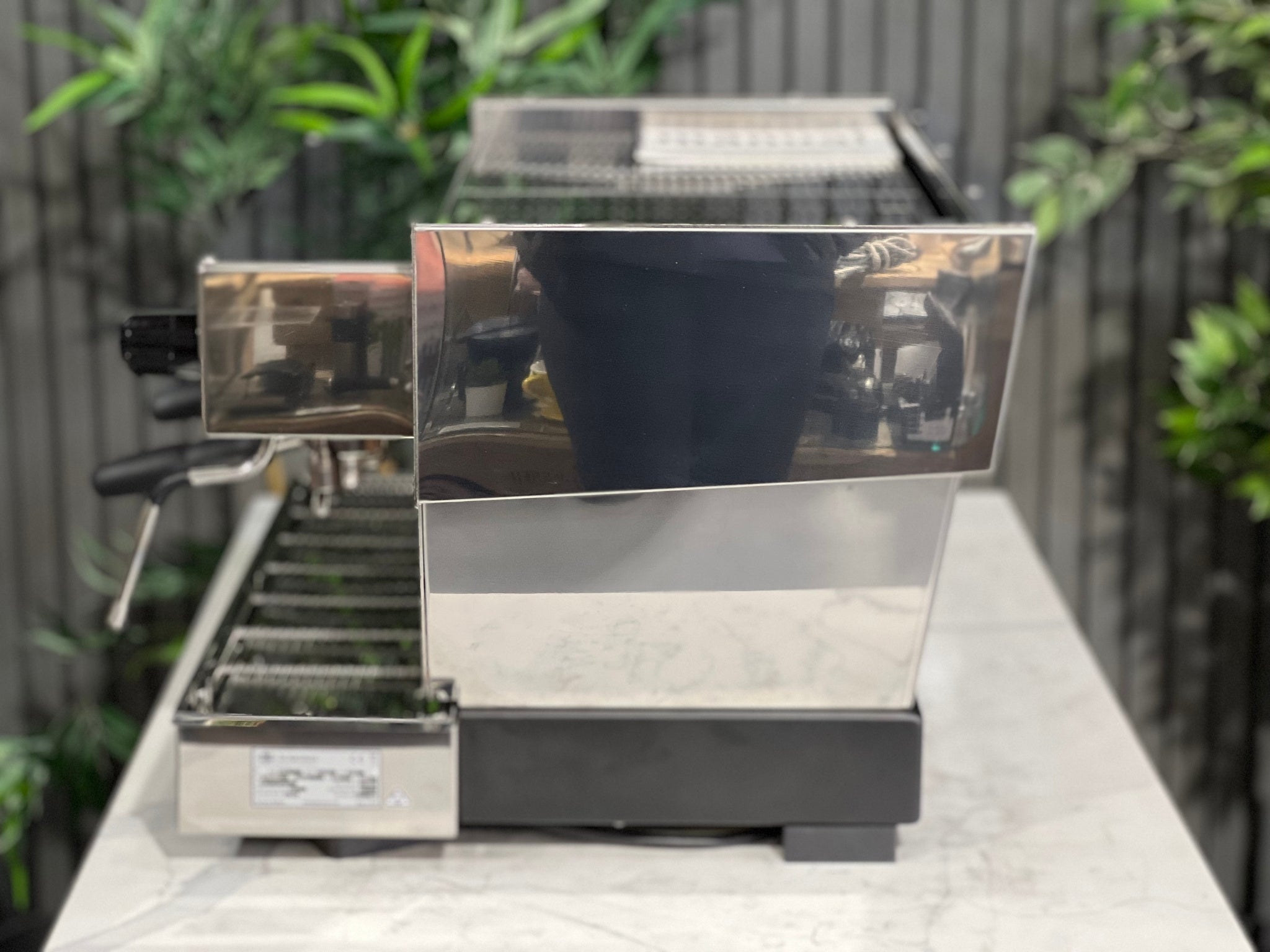 La Marzocco Linea Classic S AV 2 Group Coffee Machine Stainless - New side view highlighting the sleek stainless steel body, steam wand, and overall espresso performance features, displayed on a marble bench with greenery in the background.