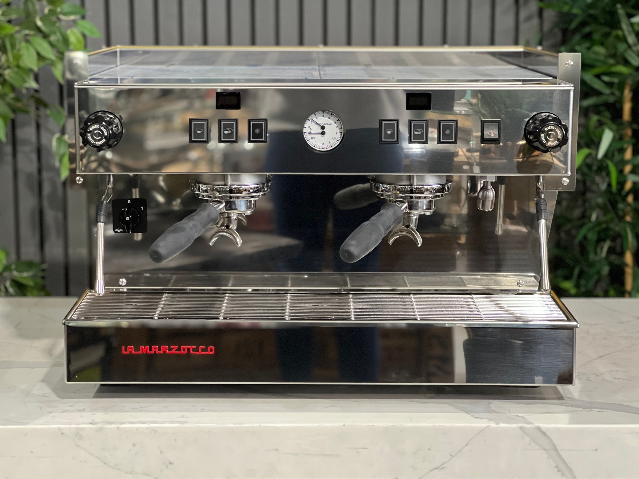 A new La Marzocco Linea Classic S AV 2 Group Coffee Machine in Yellow sitting on a marble bench. There is greenery in the background. The image is taken from the front of the machine so that you can see the front of the machine, control panel, buttons and group heads.
