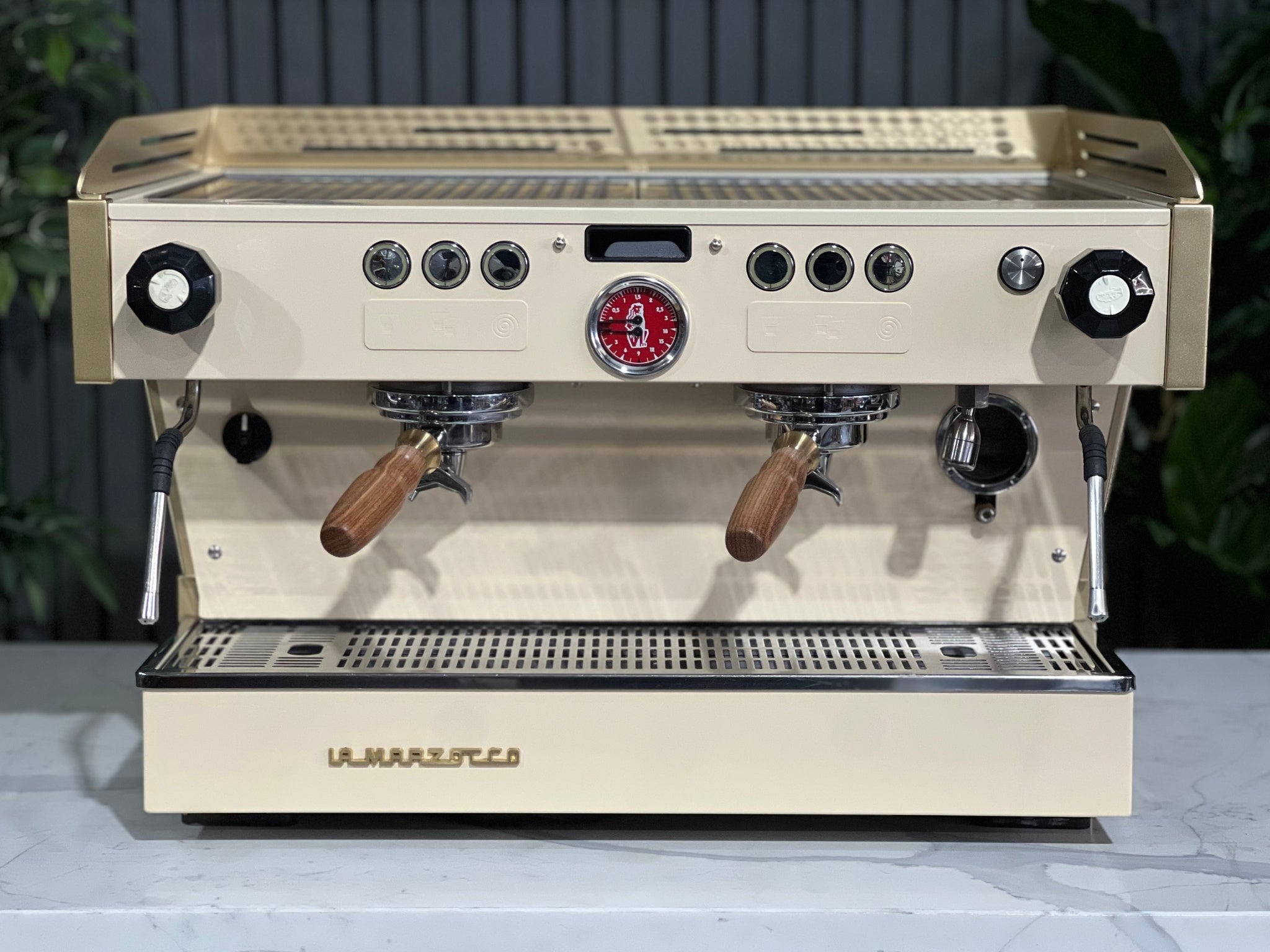 La Marzocco Linea PB 2 Group Coffee Machine Cream & Gold - Used photographed front-on on a marble bench with greenery visible. The espresso coffee machine displays its dual group heads, digital LED screen, and easy-to-use interface.