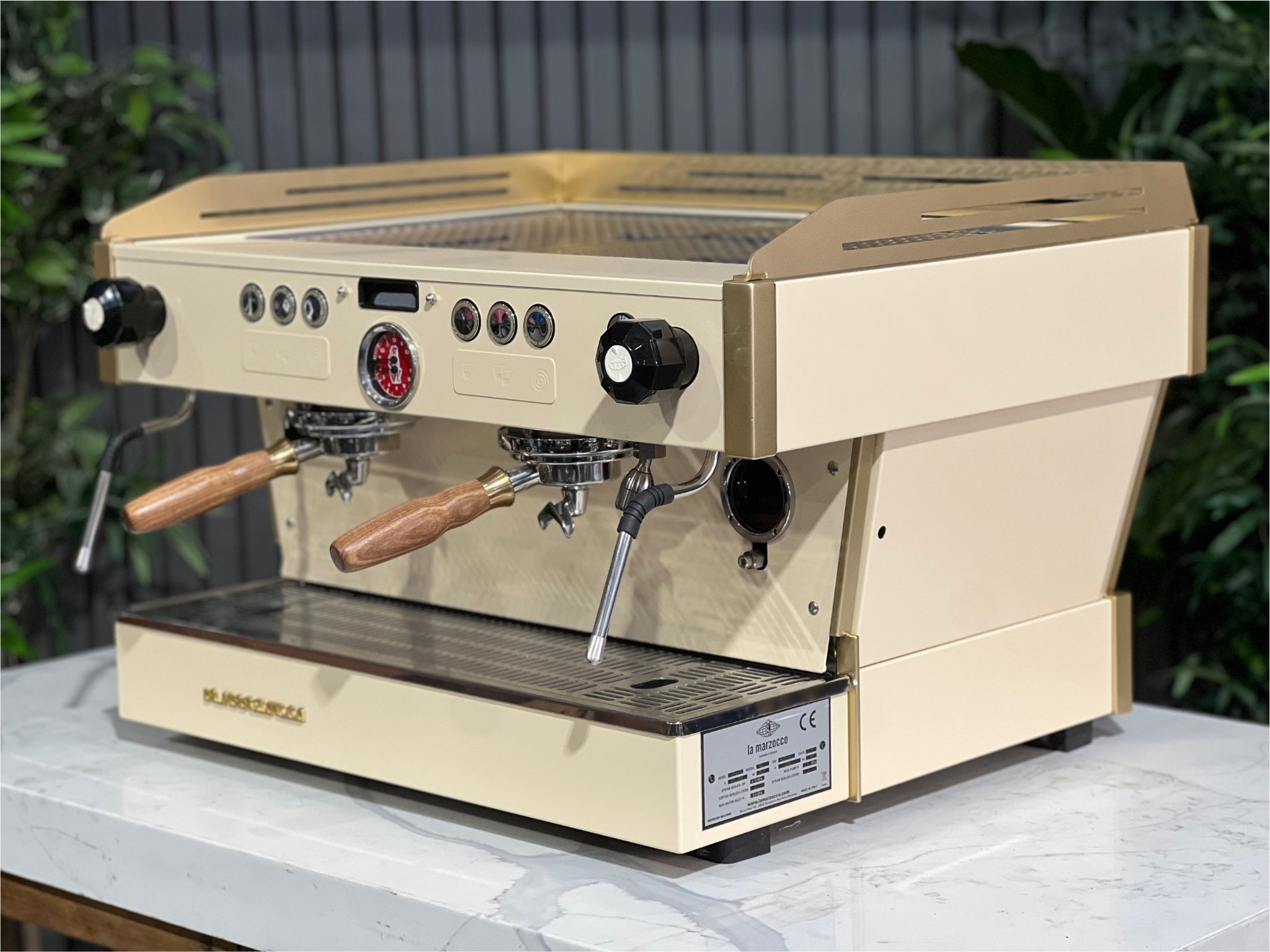 La Marzocco Linea PB 2 Group Coffee Machine Cream & Gold - Used shown at an angle on a marble bench with greenery in the background. This espresso machine features a striking cream and gold body, dual group heads, and digital controls for professional espresso performance.
