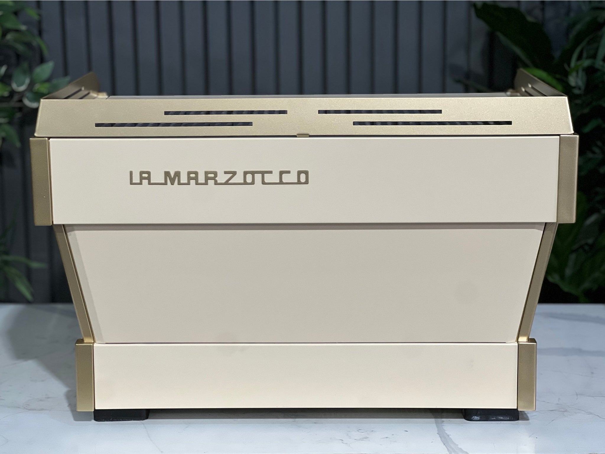 La Marzocco Linea PB 2 Group Coffee Machine Cream & Gold - Used shown from the back on a marble bench with greenery in the background. The rear panel of the espresso machine highlights its cream and gold finish, ideal for stylish café setups.