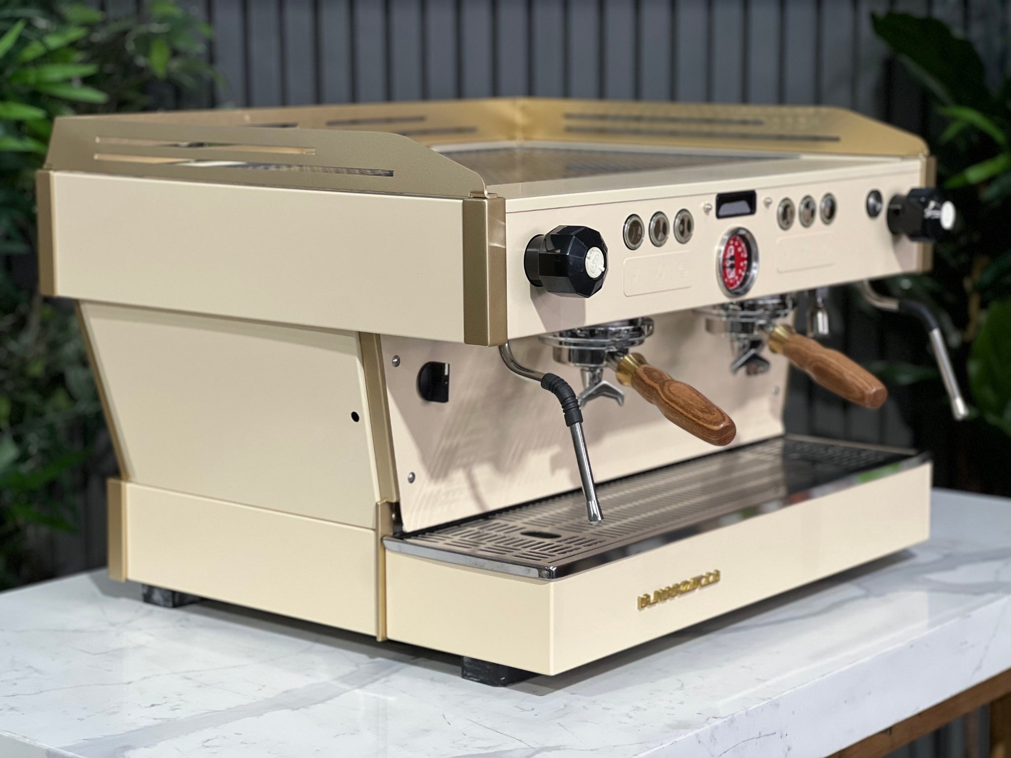 La Marzocco Linea PB 2 Group Coffee Machine Cream & Gold - Used shown at an angle on a marble bench with greenery in the background. This espresso machine features a striking cream and gold body, dual group heads, and digital controls for professional espresso performance.