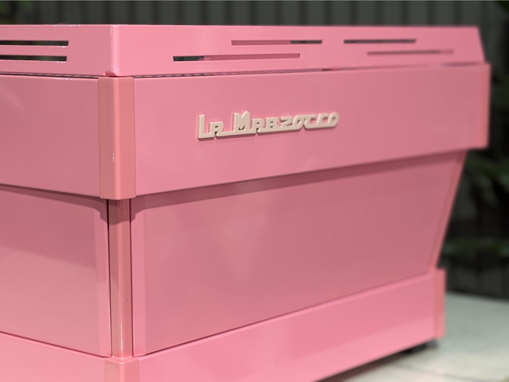 La Marzocco Linea PB 2 Group Coffee Machine Dark Pink close-up back angled view showcasing the flat rear panel, sharp edges, and industrial design of this commercial espresso coffee machine, positioned on a marble bench with greenery in the background.