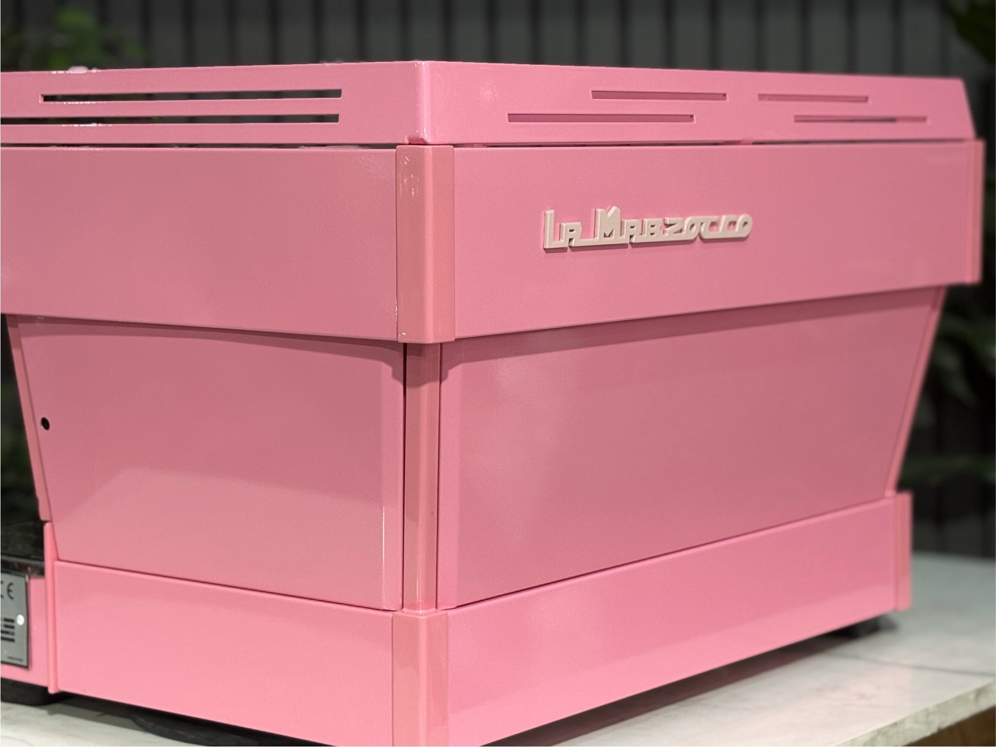 La Marzocco Linea PB 2 Group Coffee Machine Dark Pink close-up back angled view showcasing the flat rear panel, sharp edges, and industrial design of this commercial espresso coffee machine, positioned on a marble bench with greenery in the background.