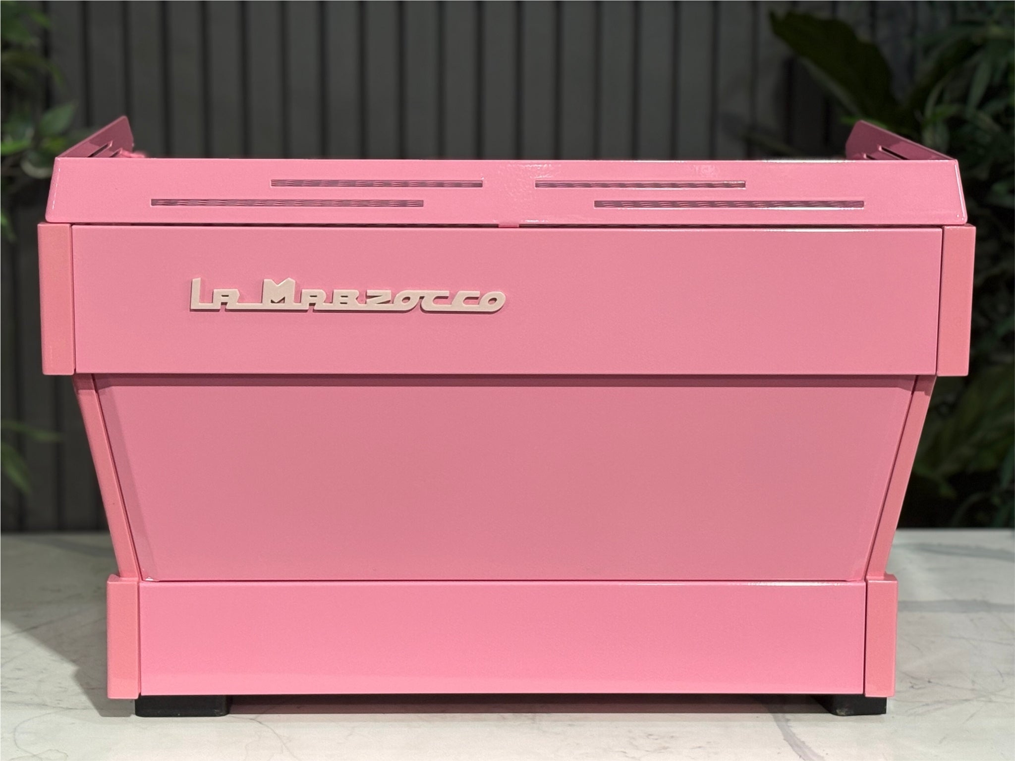 La Marzocco Linea PB 2 Group Coffee Machine Dark Pink rear view featuring the smooth custom-painted pink back panel and defined shape of this high-performance espresso coffee machine, placed on a marble bench with a garden setting in the background.