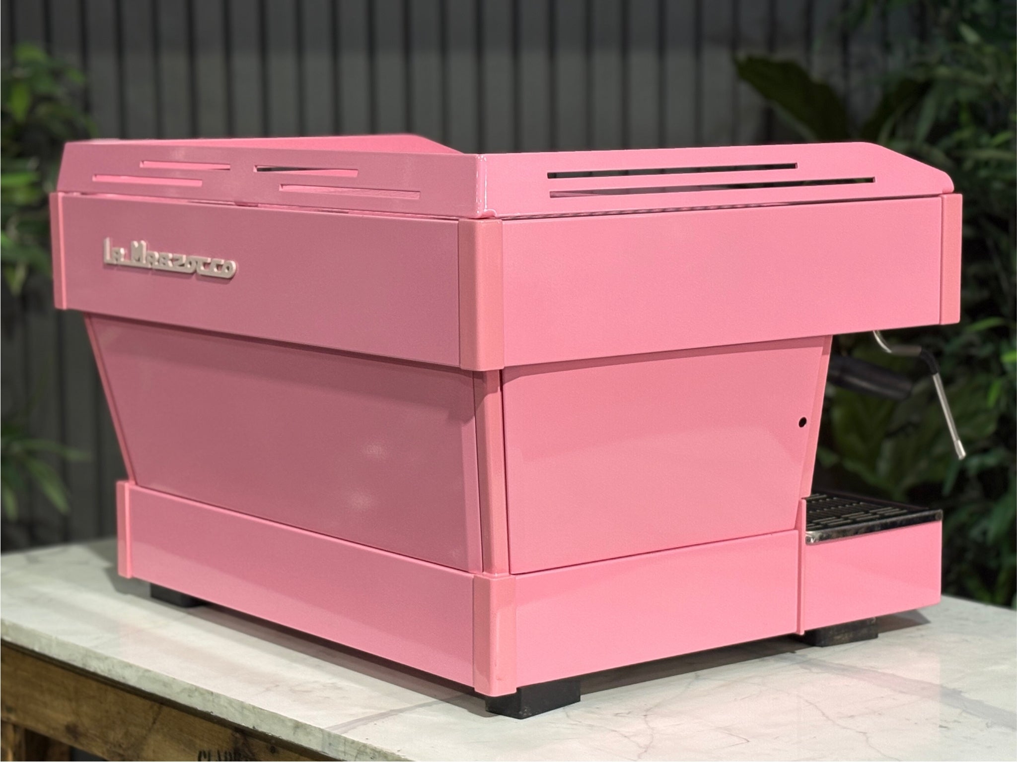 La Marzocco Linea PB 2 Group Coffee Machine Dark Pink rear-angled view showing the sleek lines of the custom pink body and rear panel, ideal for espresso performance in a café setting, with greenery behind.