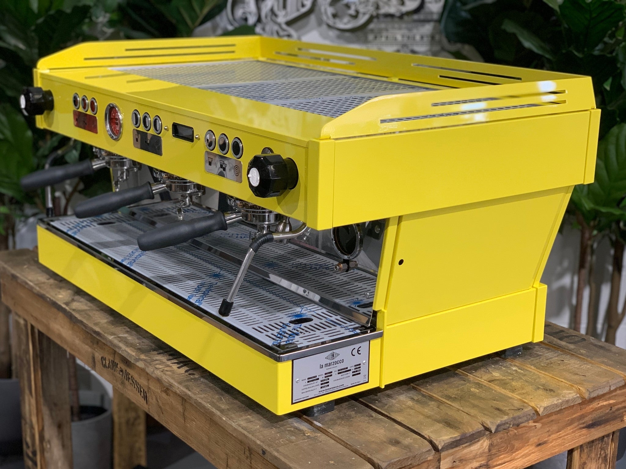 La Marzocco Linea PB 3 Group Coffee Machine Yellow – New espresso coffee machine angled view on a wooden bench with greenery, showing group heads, dual steam wands, cup tray, and LED display.