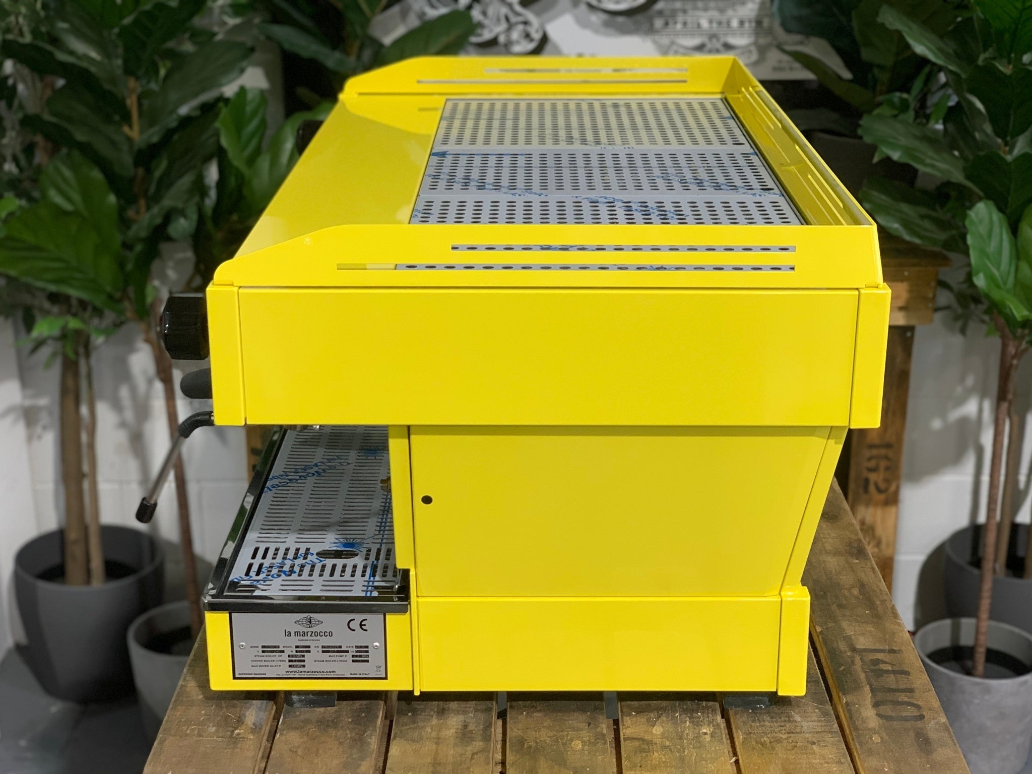 La Marzocco Linea PB 3 Group Coffee Machine Yellow – New espresso coffee machine side view on wooden bench with greenery, displaying yellow body, stainless finish, steam wand, and machine depth.