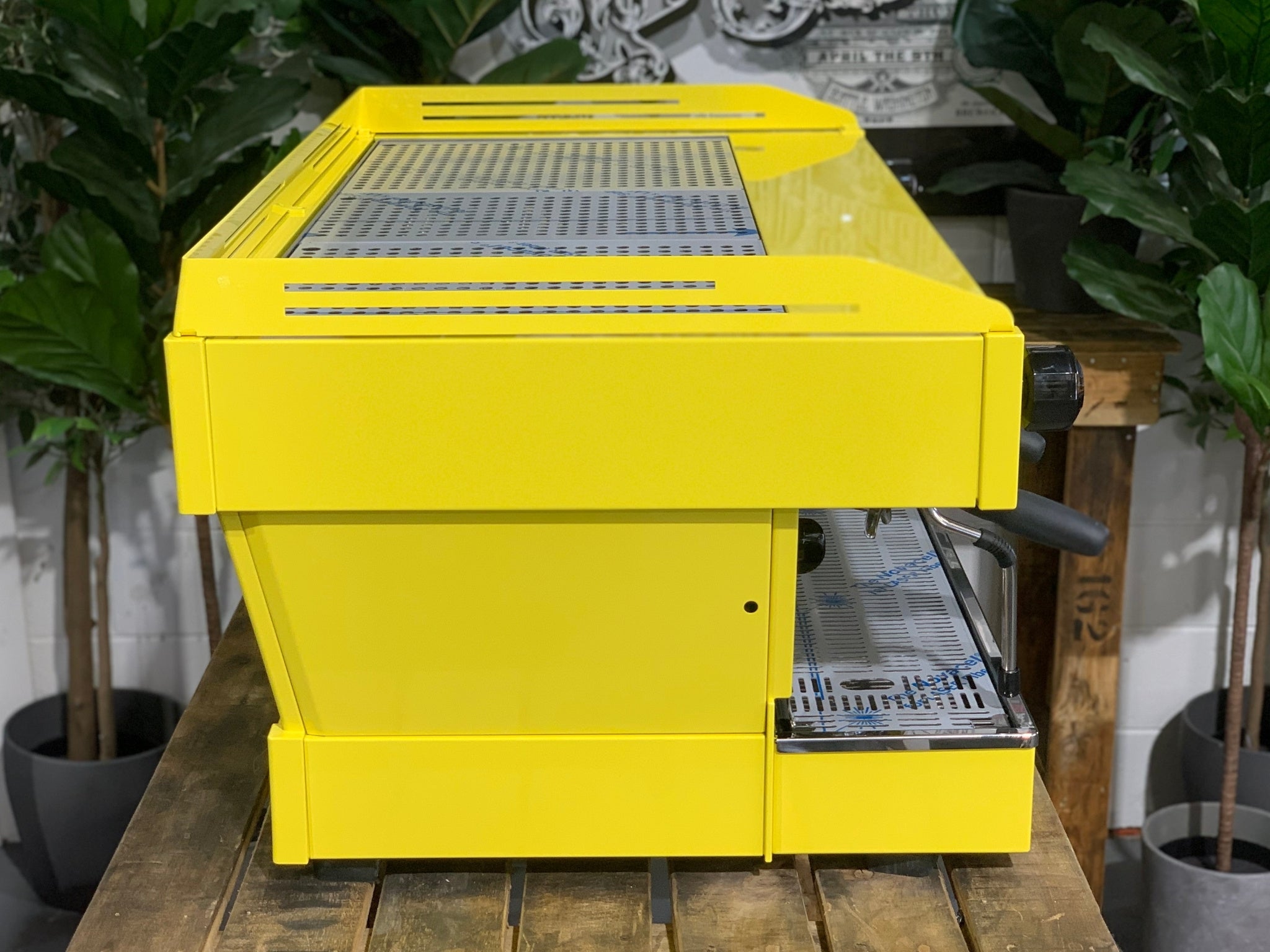 La Marzocco Linea PB 3 Group Coffee Machine Yellow – New espresso coffee machine side view on wooden bench with greenery, displaying yellow body, steam wand, and machine depth.
