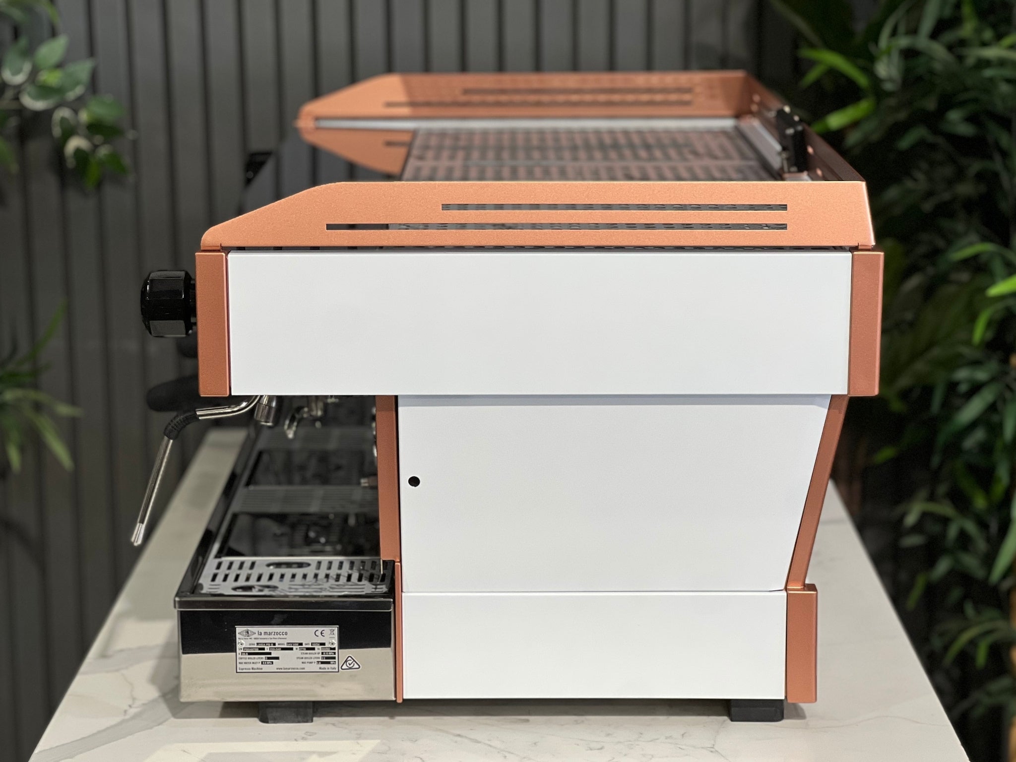 La Marzocco Linea PB ABR 3 Group Coffee Machine White & Copper - New side view highlighting the white body, copper accents, one dual steam wand, and part of the digital display, placed on a marble bench with greenery in the background.