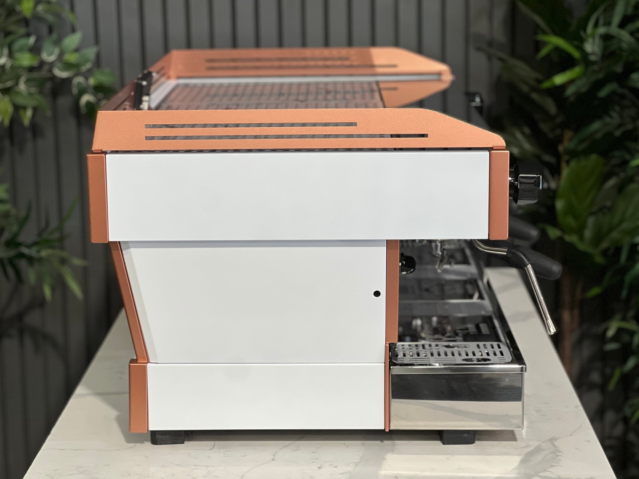 La Marzocco Linea PB ABR 3 Group Coffee Machine White & Copper - New side view highlighting the white body, copper accents, one dual steam wand, and part of the digital display, placed on a marble bench with greenery in the background.