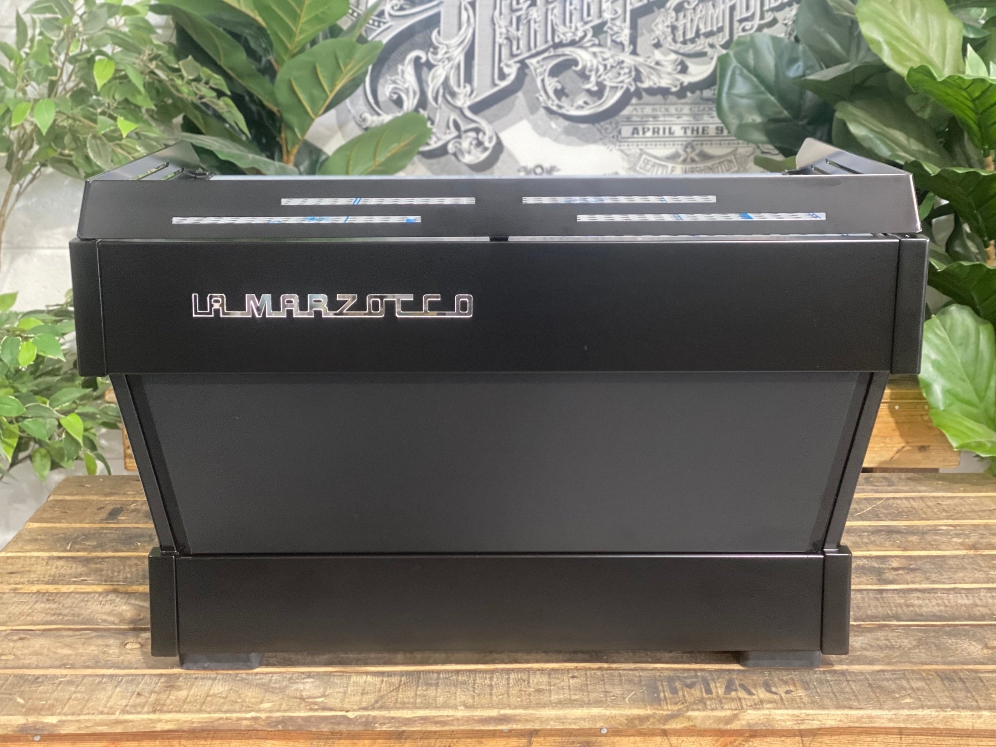La Marzocco Linea PB 2 Group Coffee Machine Black - New back view showing the espresso machine’s black stainless steel body panels and rear structure, placed on a wooden bench with greenery in the background.