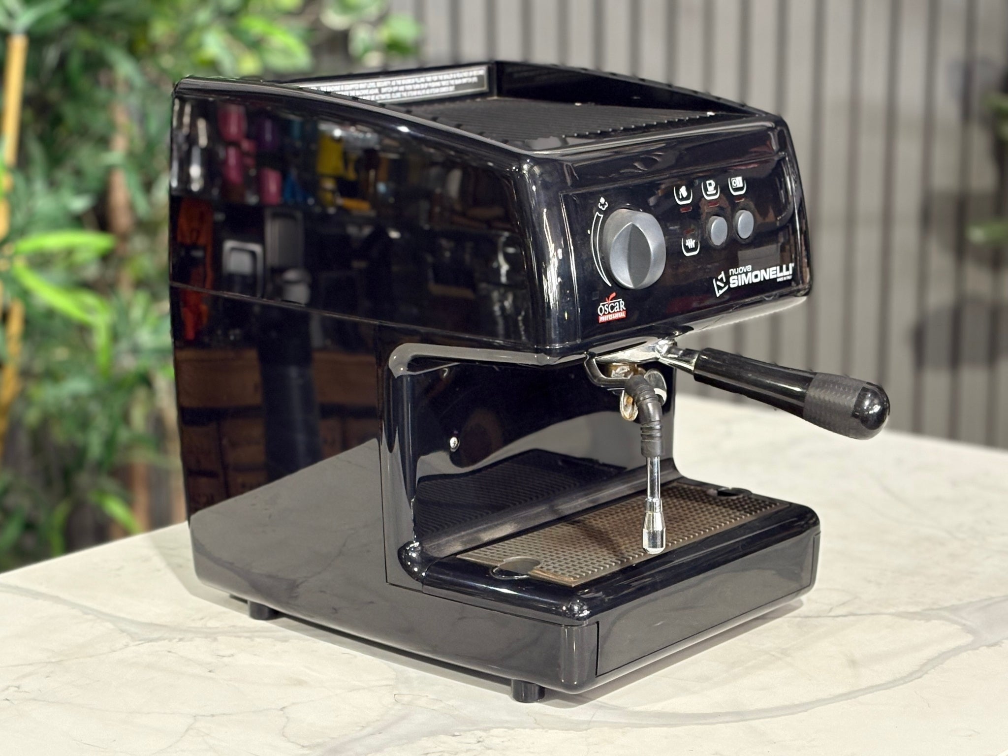 Nuova Simonelli Oscar Professional 1 Group Coffee Machine Black - Used espresso machine pictured from the side, showing the machine’s slim profile, black finish, and protruding steam wand. Placed on a marble bench with greenery visible behind.
