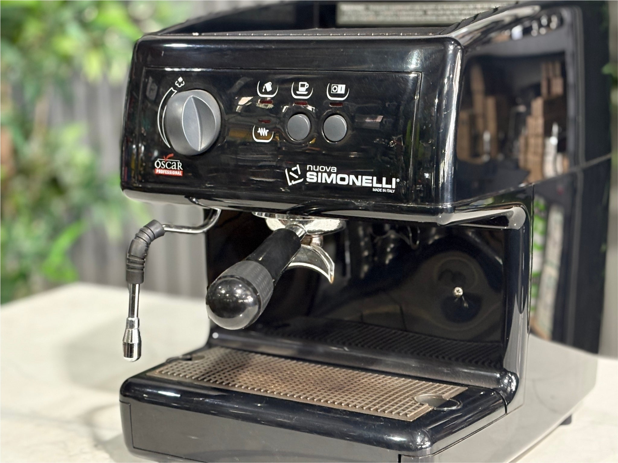 Close-up of the Nuova Simonelli Oscar Professional 1 Group Coffee Machine Black - Used espresso machine, focusing on the group head, steam knob, and cup tray. Captured on a marble bench with greenery behind.