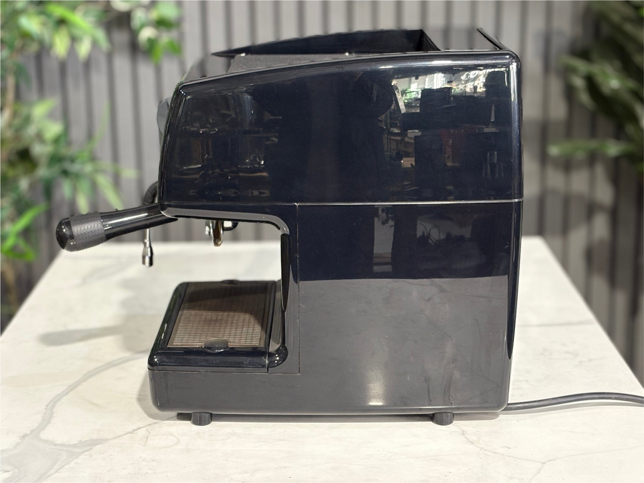 Nuova Simonelli Oscar Professional 1 Group Coffee Machine Black - Used espresso machine pictured from the side, showing the machine’s slim profile, black finish, and protruding steam wand. Placed on a marble bench with greenery visible behind.