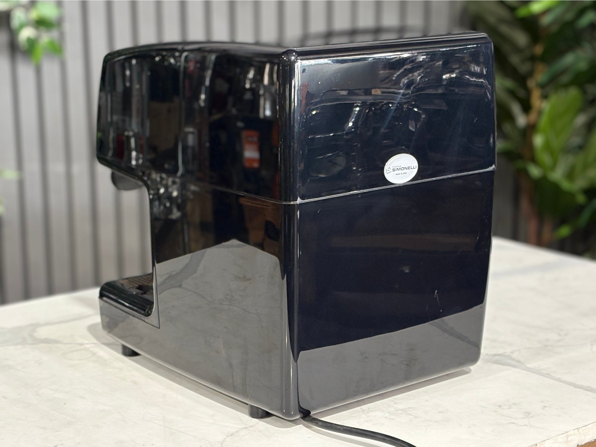 Nuova Simonelli Oscar Professional 1 Group Coffee Machine Black - Used espresso coffee machine viewed from the rear angle, highlighting the body design and black exterior. Displayed on a marble bench with greenery in the background.