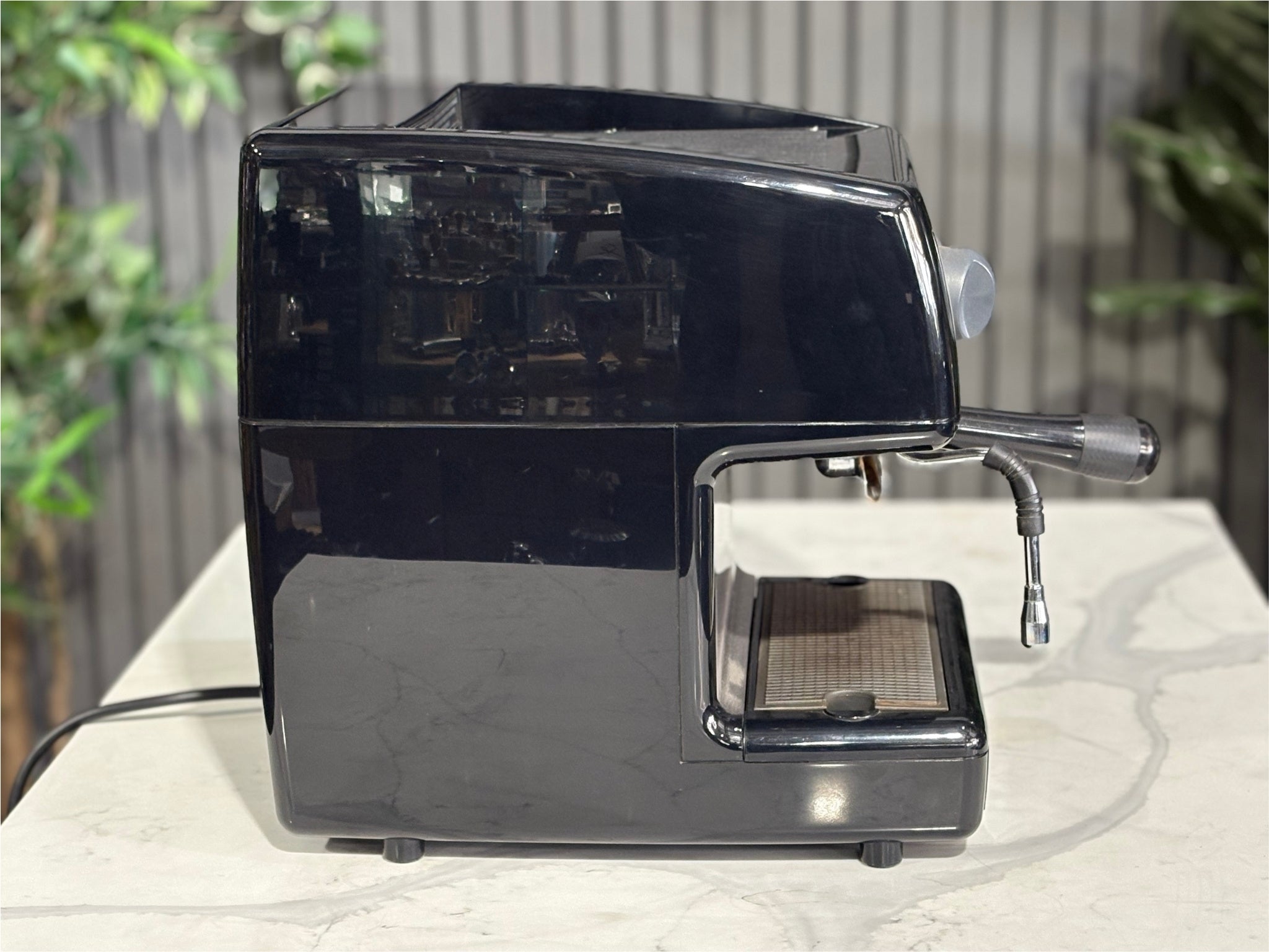 Nuova Simonelli Oscar Professional 1 Group Coffee Machine Black - Used espresso machine pictured from the side, showing the machine’s slim profile, black finish, and protruding steam wand. Placed on a marble bench with greenery visible behind.