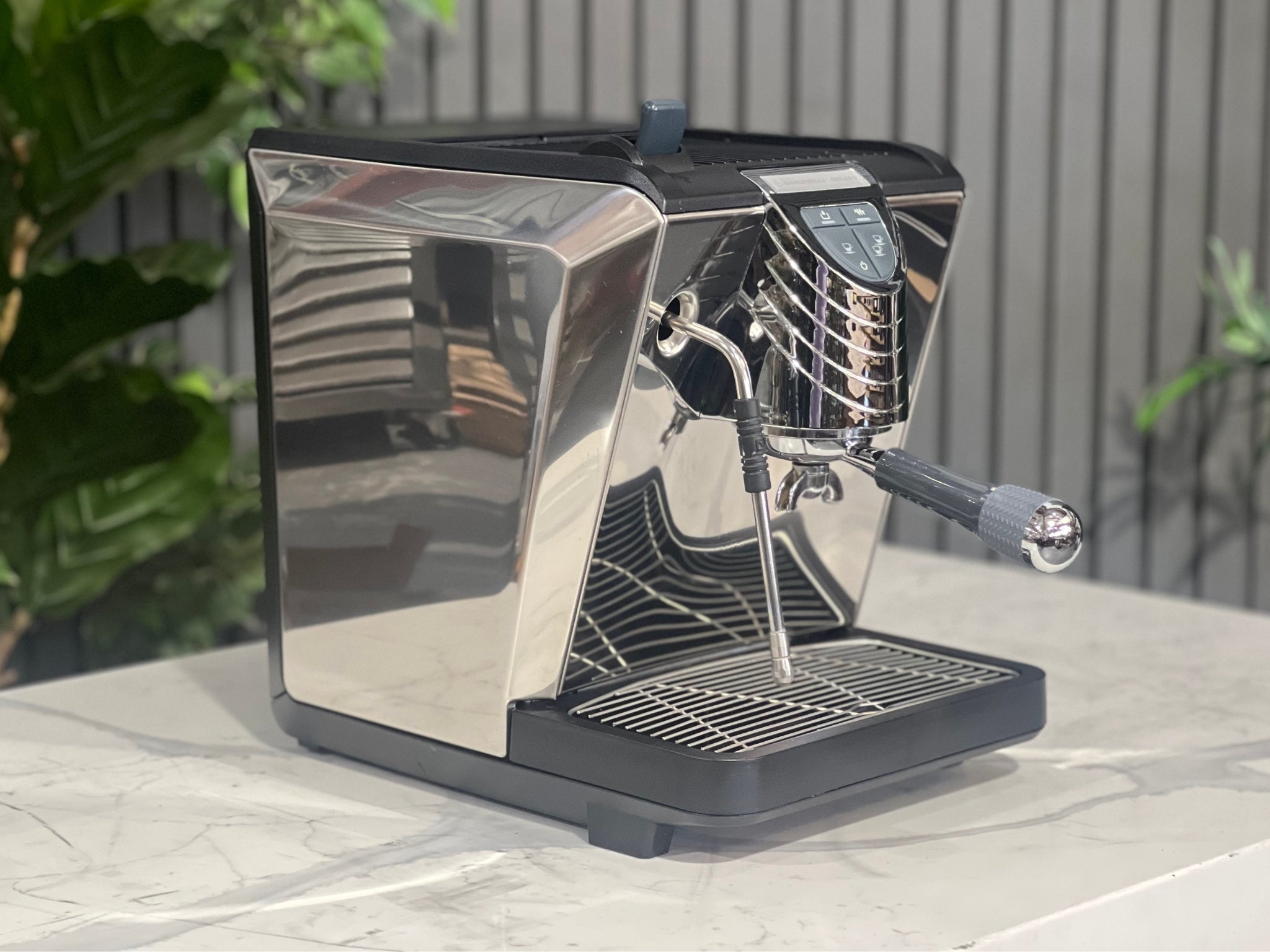 Nuova Simonelli Oscar Professional 1 Group Espresso Coffee Machine Black shown at an angle, featuring a black front panel with sleek silver sides, a commercial 58mm group head, and knob-operated steam wand, sitting on a marble bench with greenery in the background.
