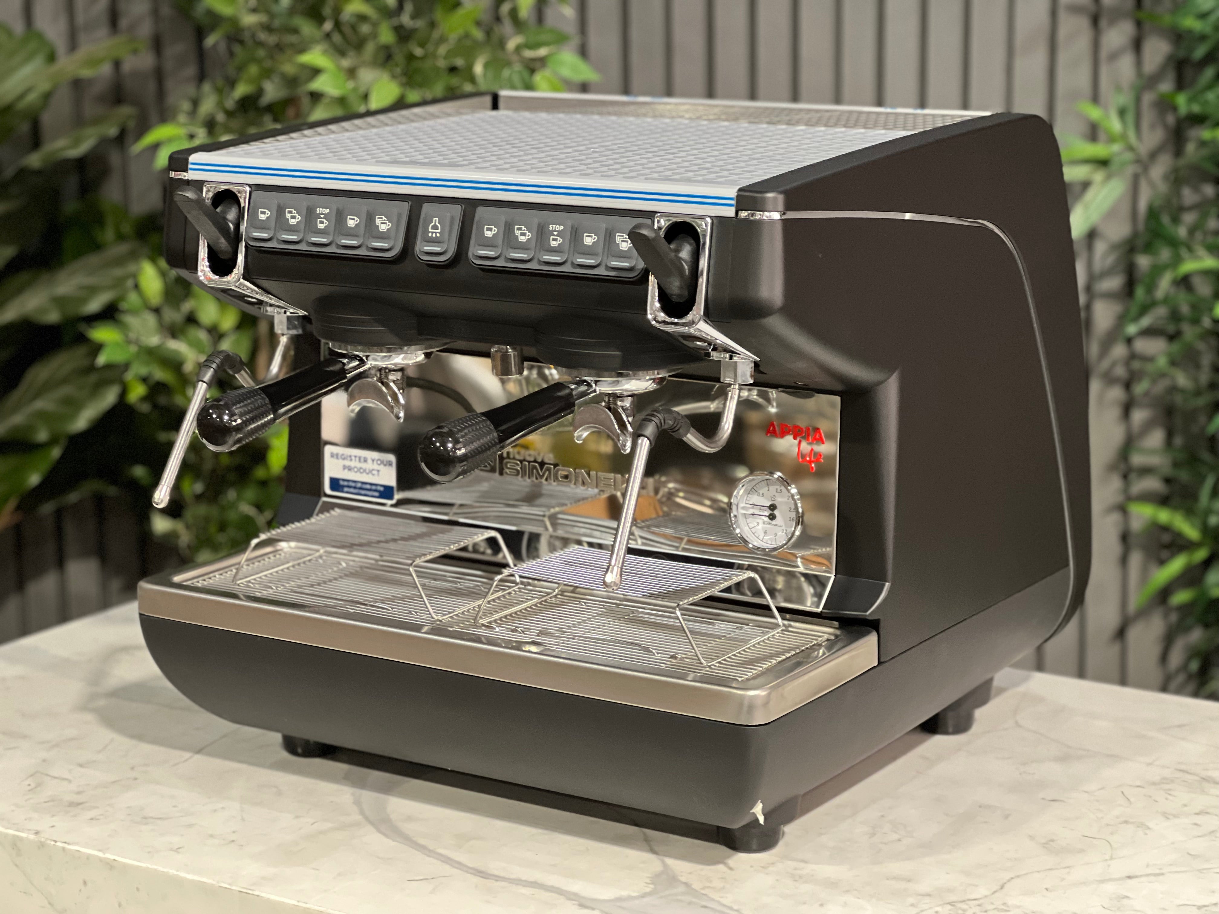 Nuova Simonelli Appia Life Compact Black 2 Group Espresso Machine on a countertop with greenery in background