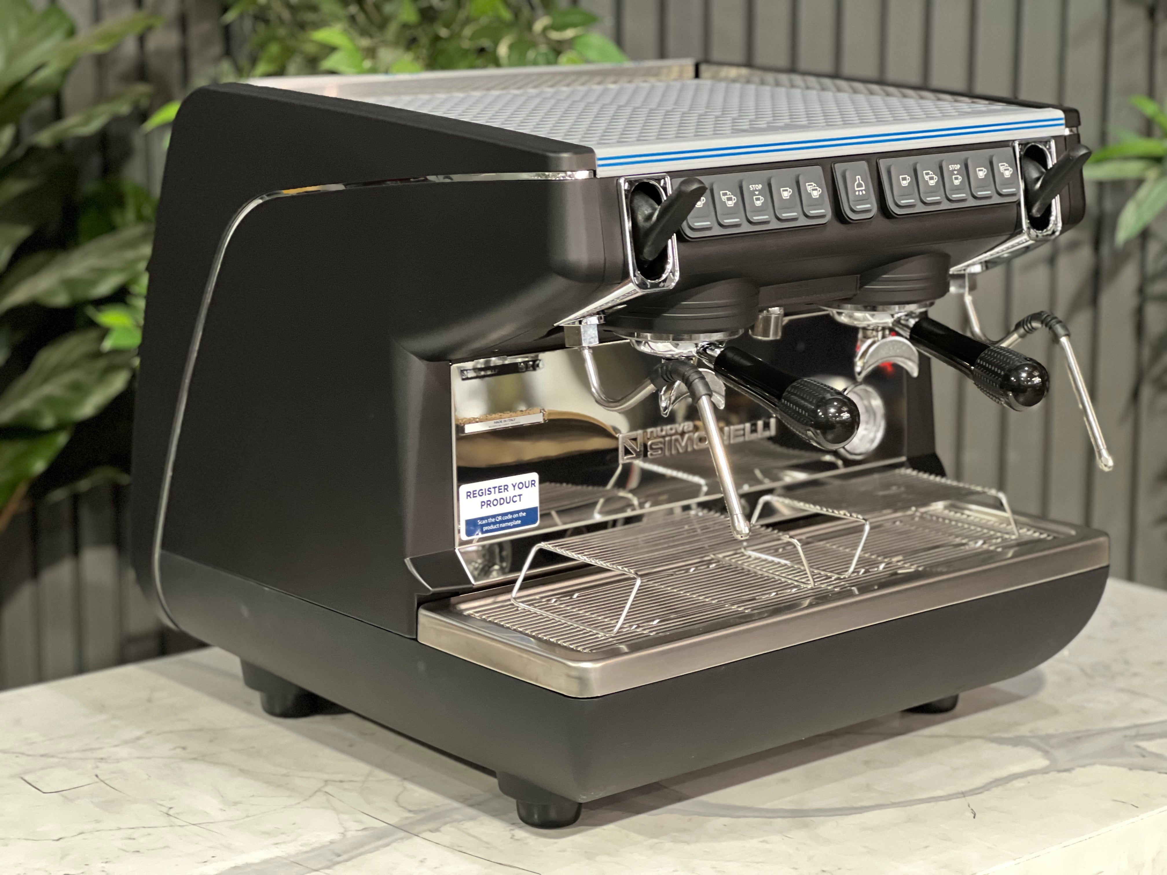 Nuova Simonelli Appia Life Compact Black 2 Group Espresso Machine on a counter with greenery in background.