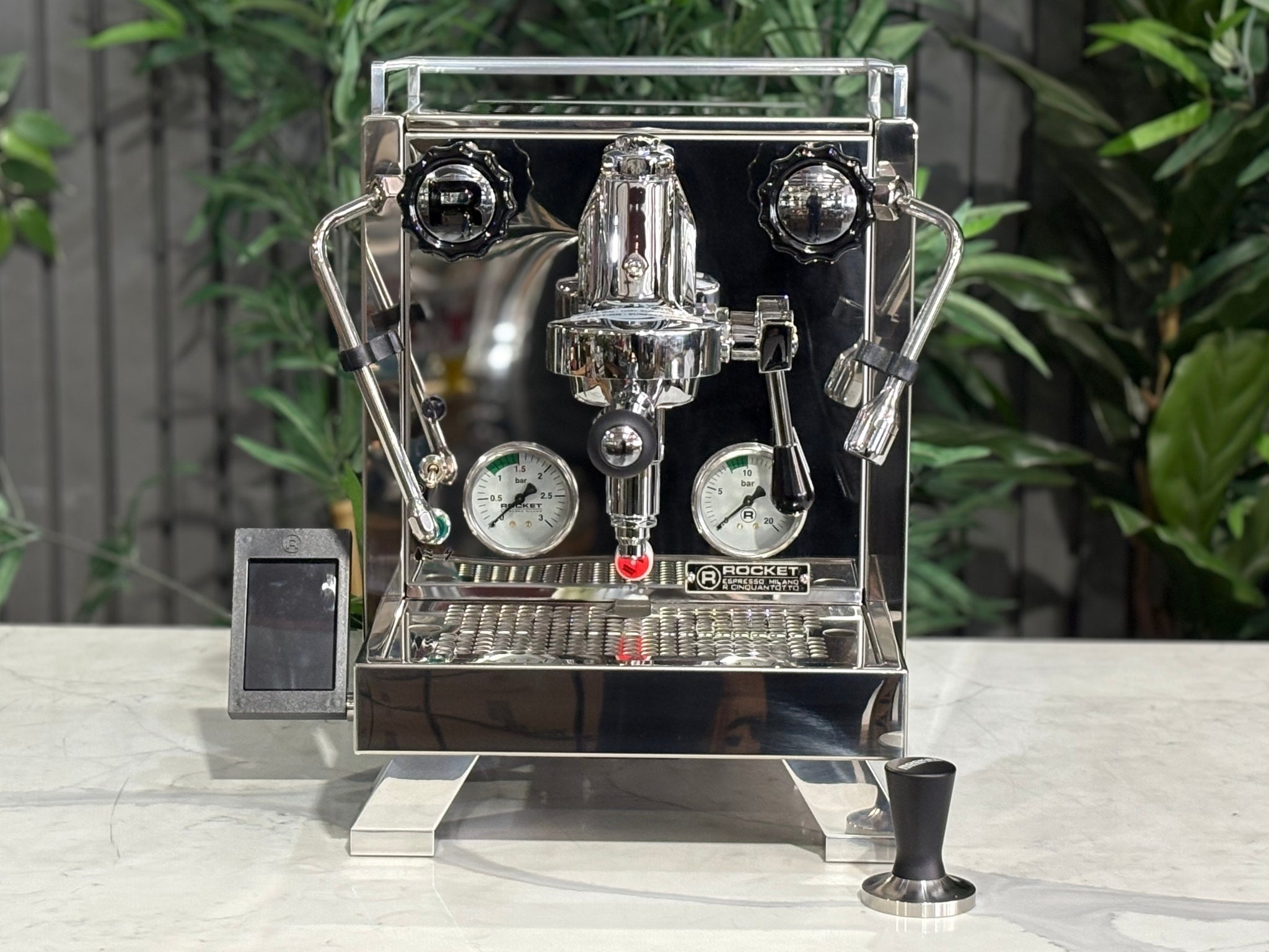 Rocket Cinquantotto R58 1 Group Coffee Machine Stainless - New front-on view highlighting the E61 group head, lever activation controls, shot timer, and clean stainless steel finish with marble bench and greenery backdrop.